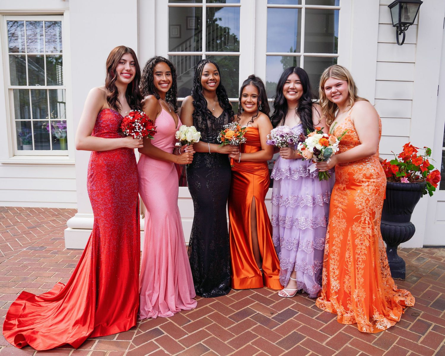 Wedding party poses in colorful formal dresses on brick patio.