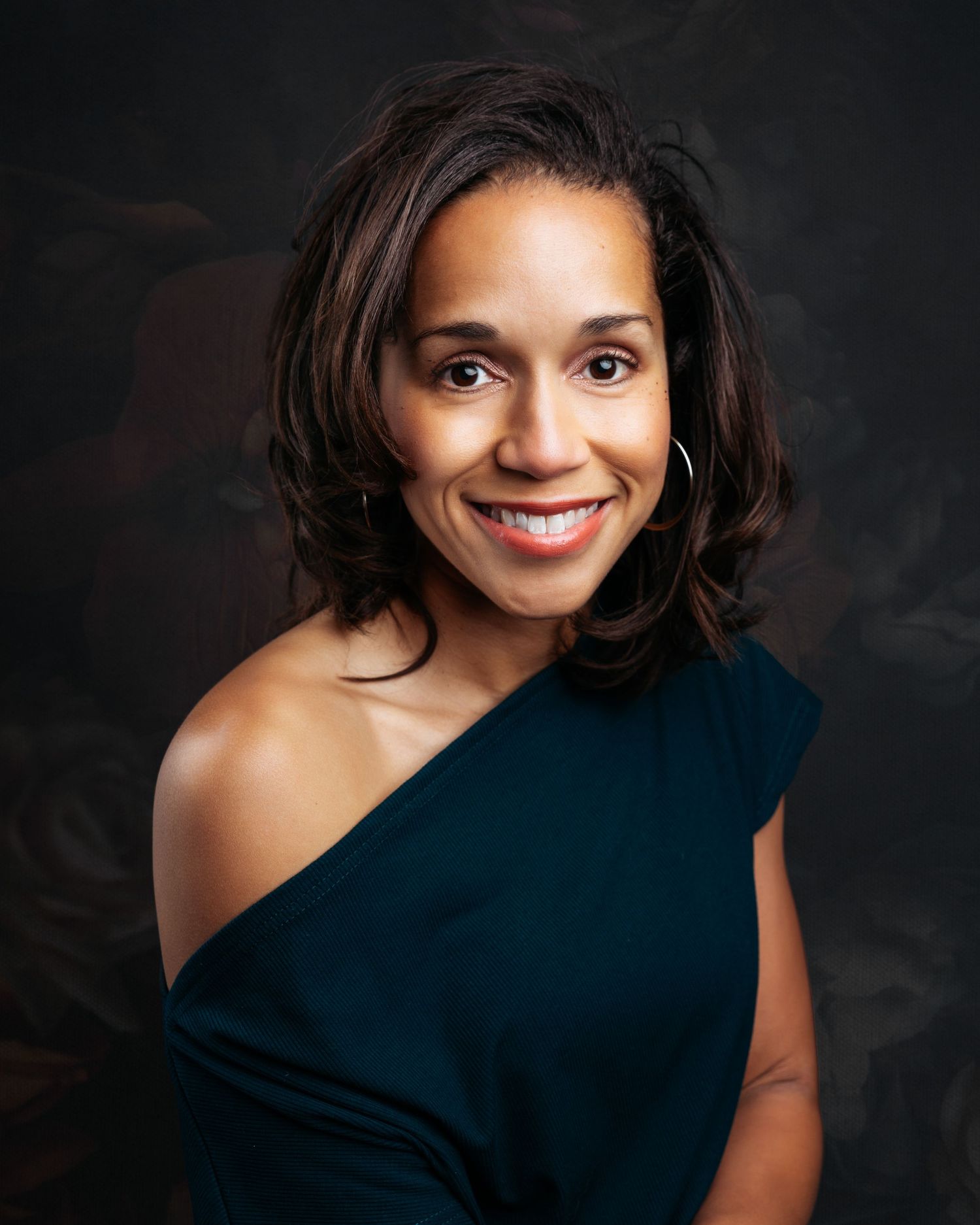 Professional headshot with asymmetrical black top against dark background.