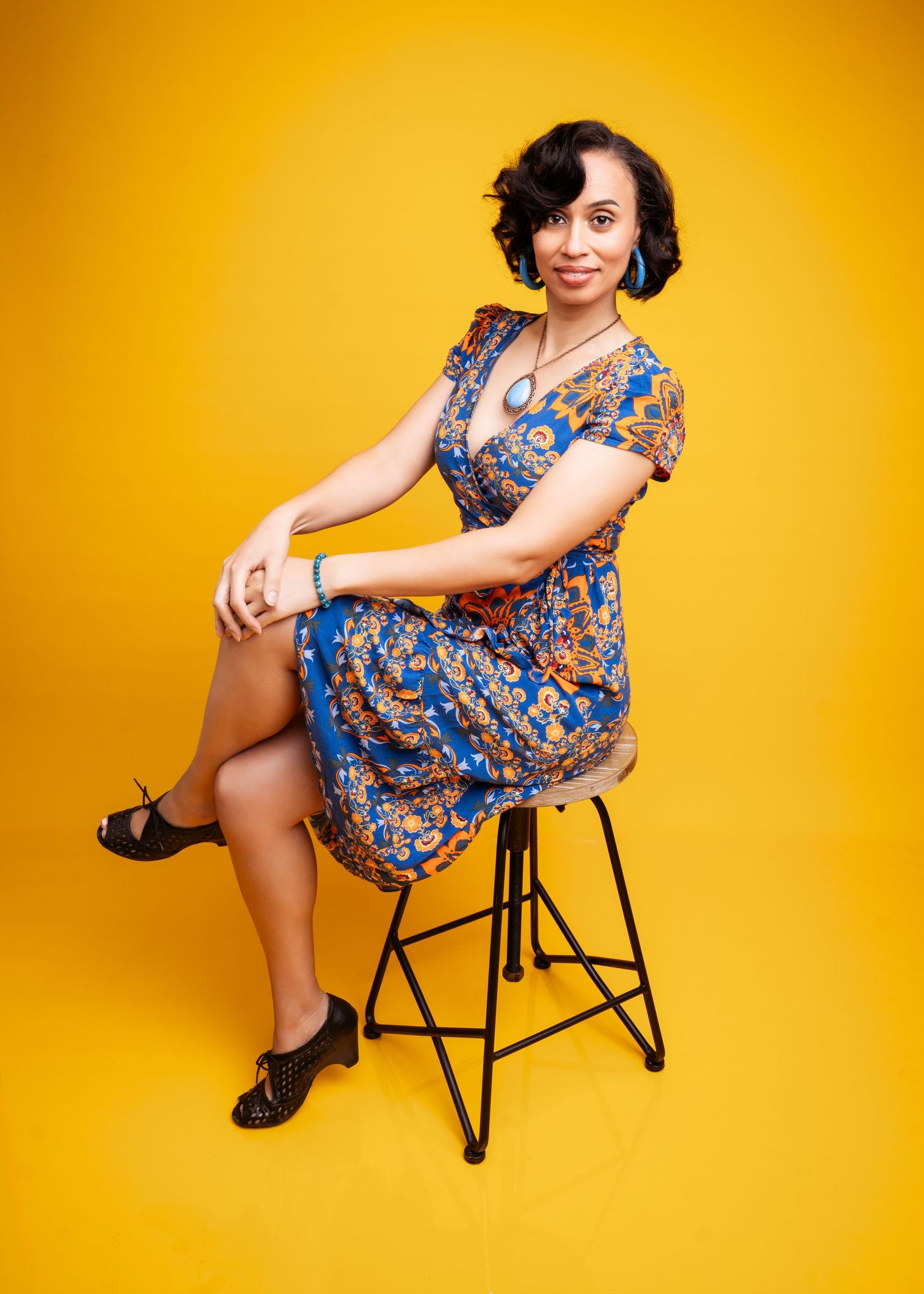 Retro-inspired floral dress pose on black chair against vibrant yellow background.