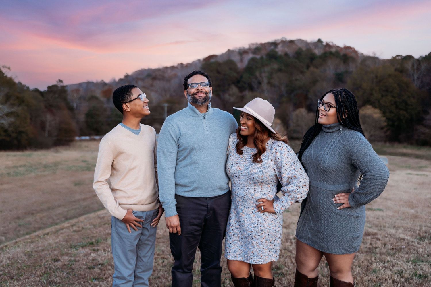 Family group poses together against a vibrant sunset sky in an outdoor field setting.