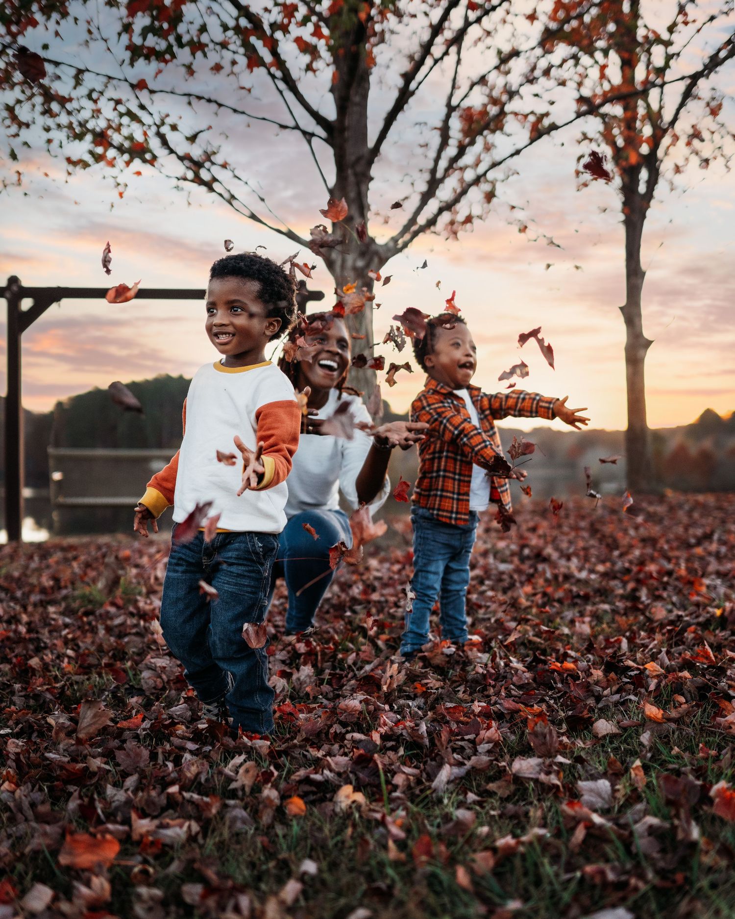 Children playing and throwing fall leaves during a golden sunset photoshoot.