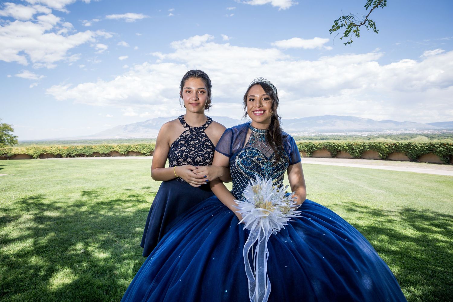 Wedding party members pose on a grassy hill under blue skies.