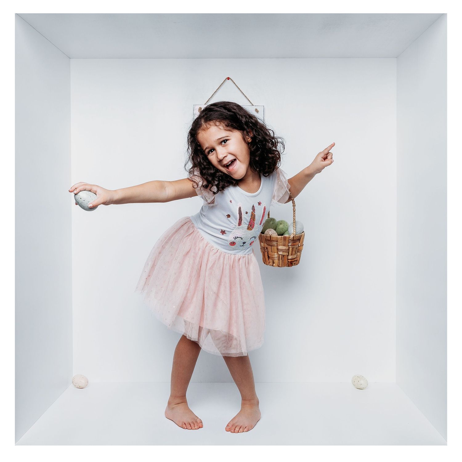 A young girl in a tulle skirt dances joyfully in a white box studio setting.