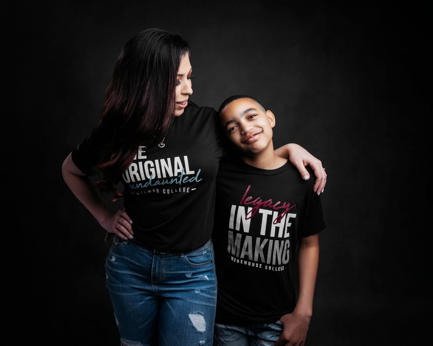 Mother and child wearing matching black t-shirts with text pose together against dark background.