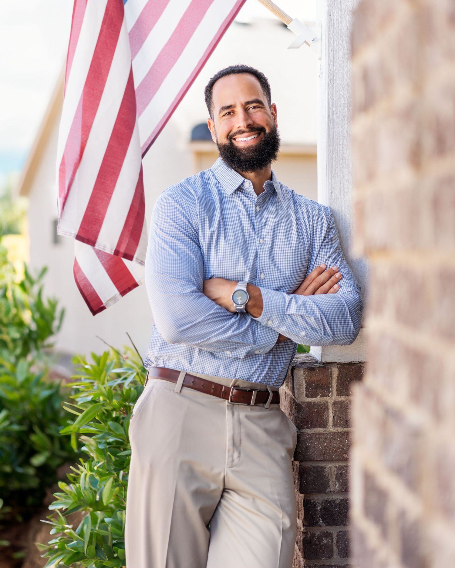Person in light blue shirt and khakis posing outdoors near American flag.