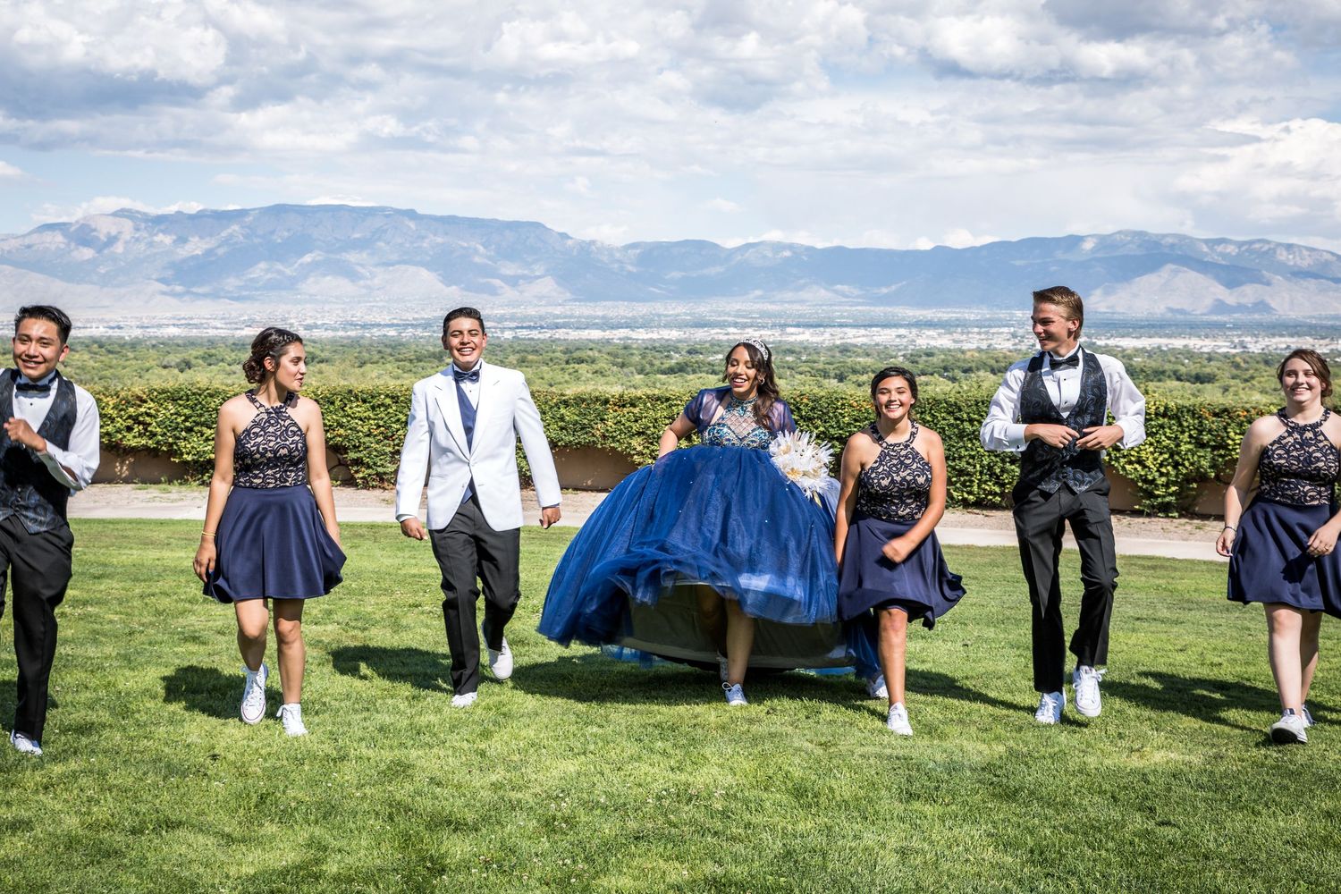 Wedding party relaxes on grass with mountains visible in the background.