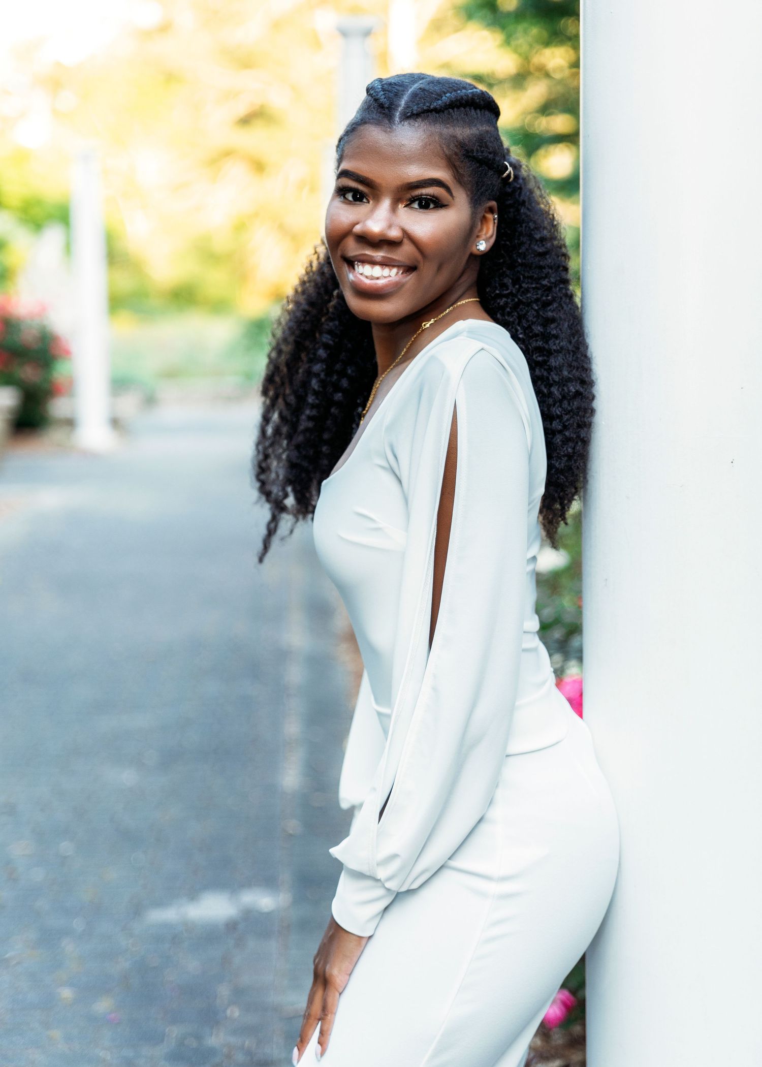 A person in a white dress poses outdoors during a photoshoot on a sunny day.