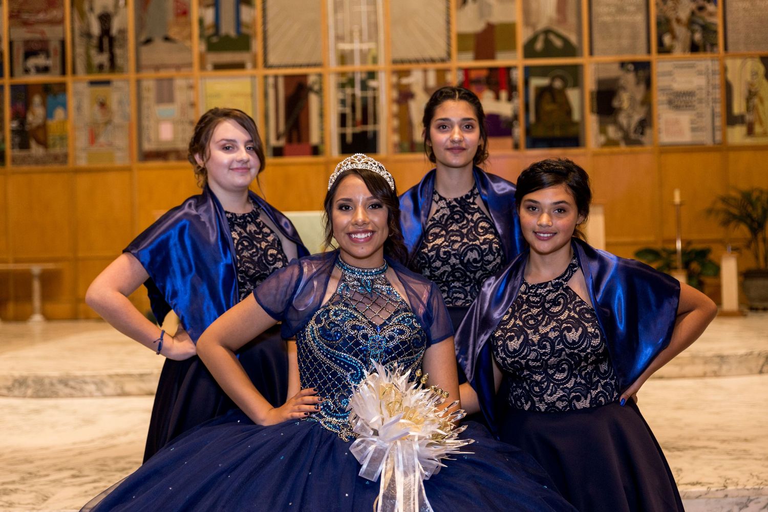 Wedding party members in navy blue attire pose together in front of a photo wall.