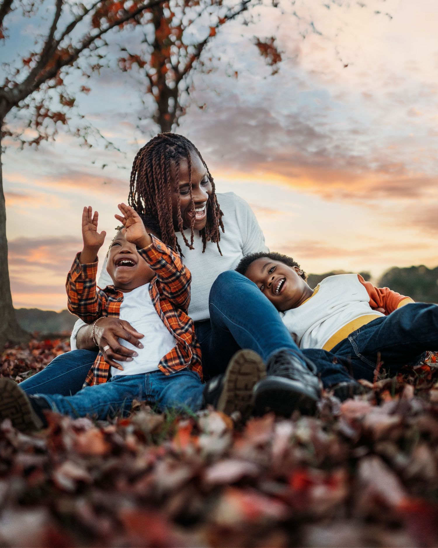 People lying in autumn leaves during sunset creating playful moments.