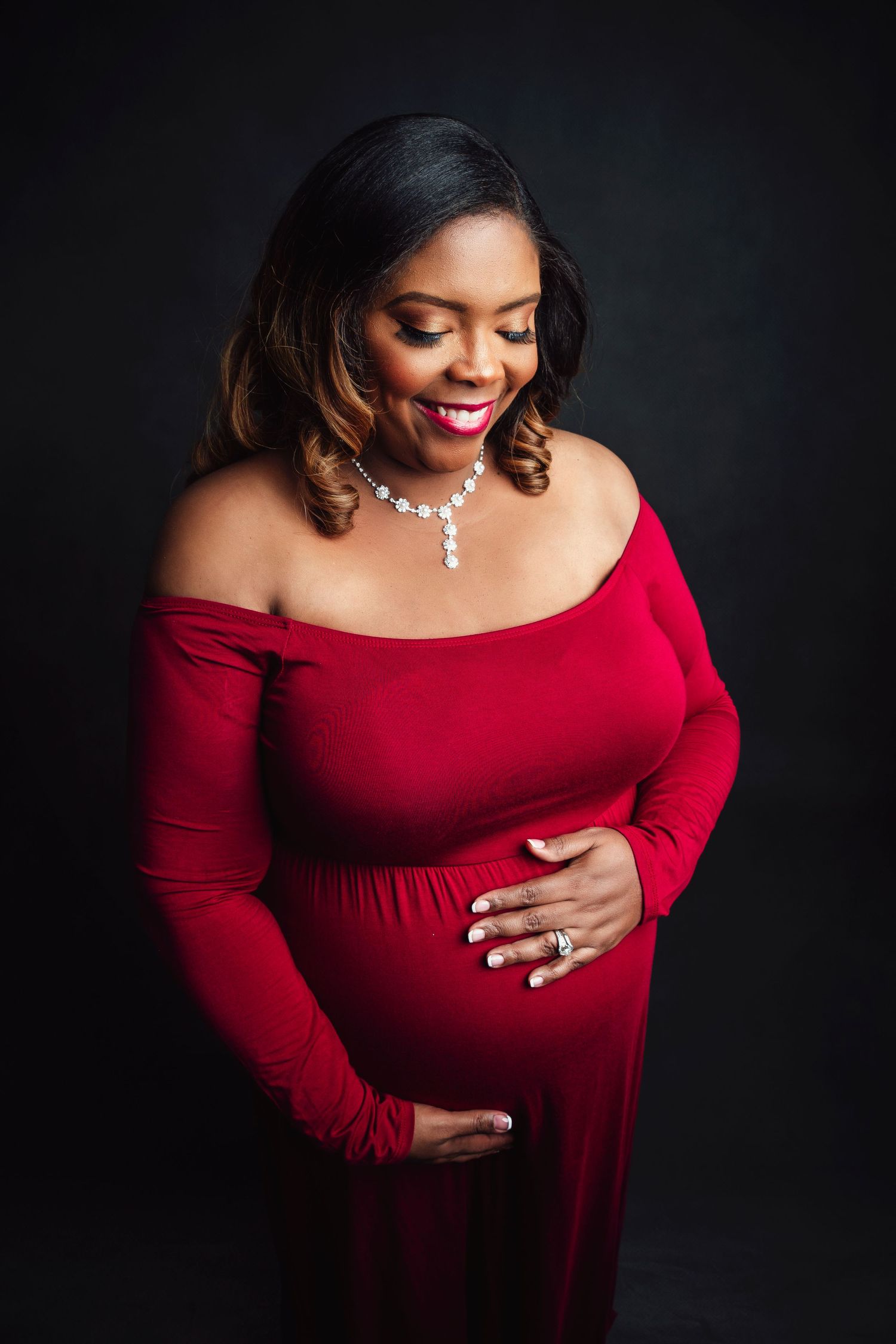 Maternity photo series showing woman in elegant red dress against dark background.