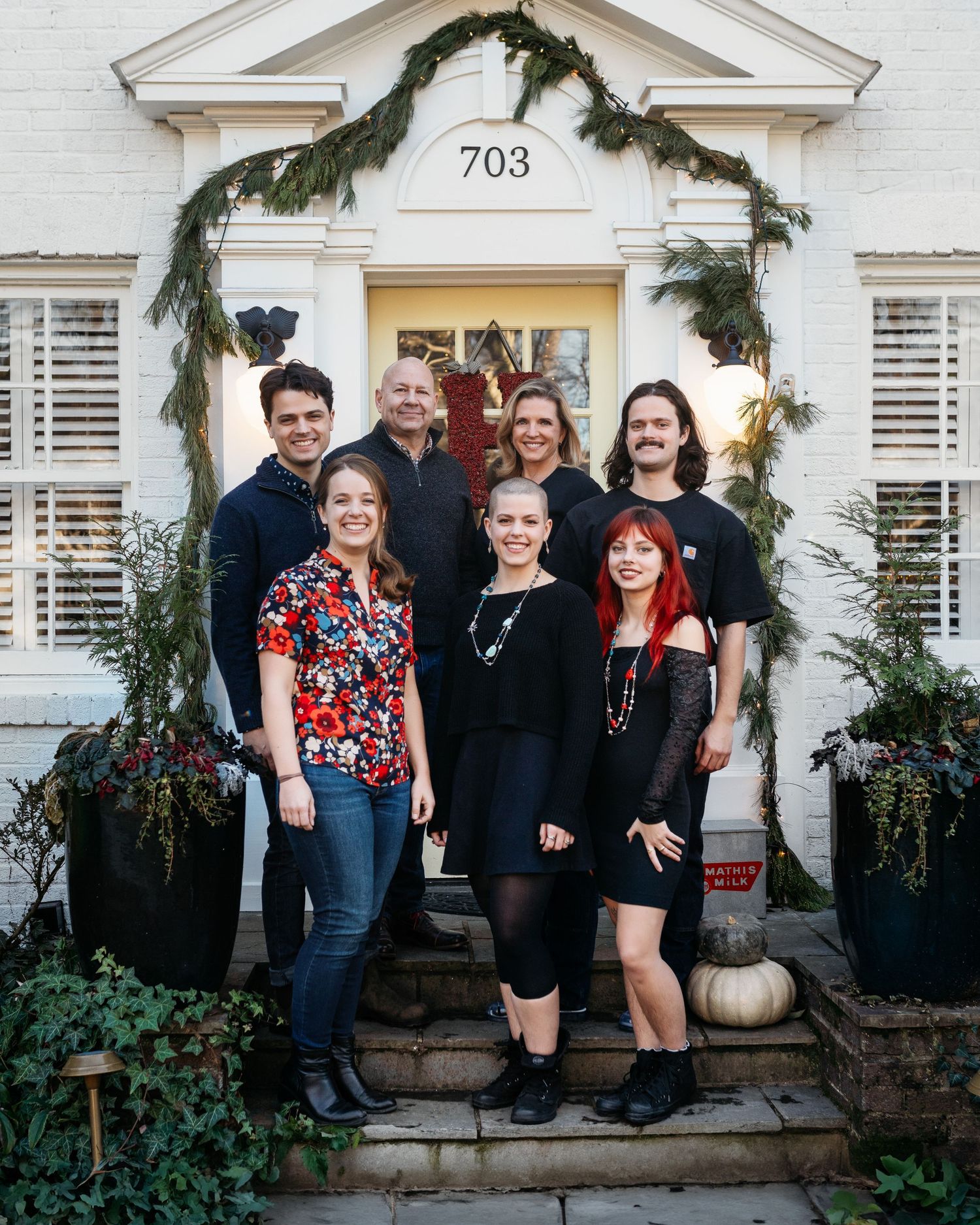 Family group photo on decorated front porch steps of white house with holiday greenery.