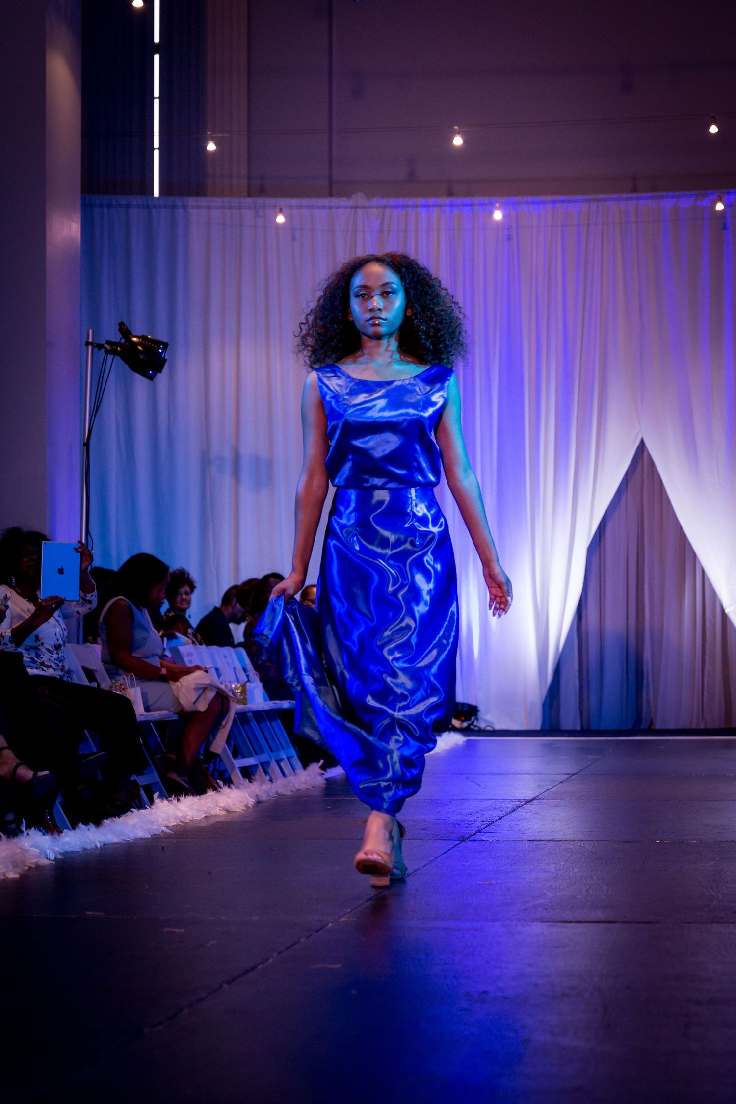 A dancer in a shiny blue dress performs a dynamic movement sequence under dramatic blue stage lighting.