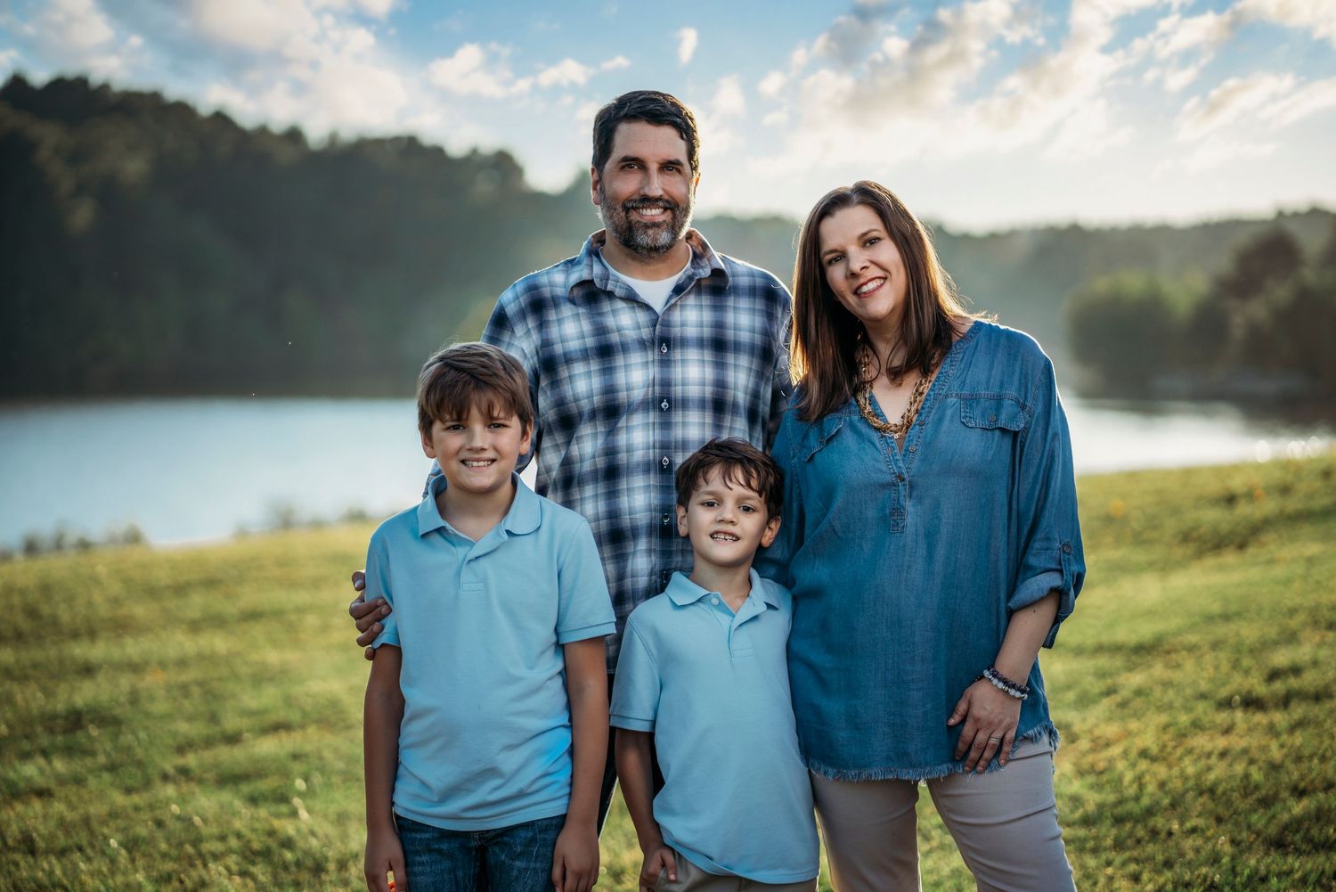 A family in coordinating blue outfits poses together on a grassy hill at sunset.