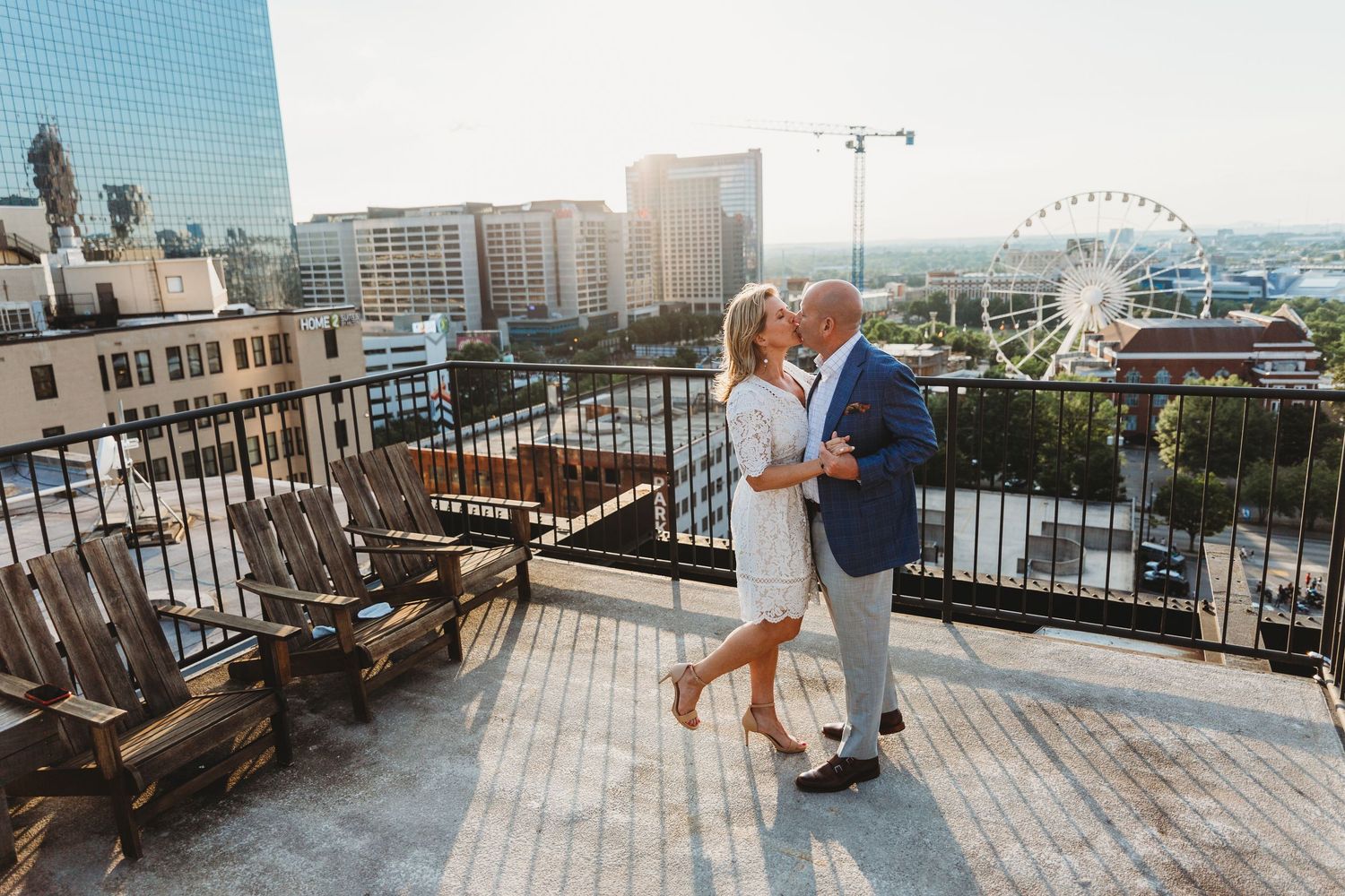 Romantic rooftop engagement photos with city skyline and ferris wheel in background.
