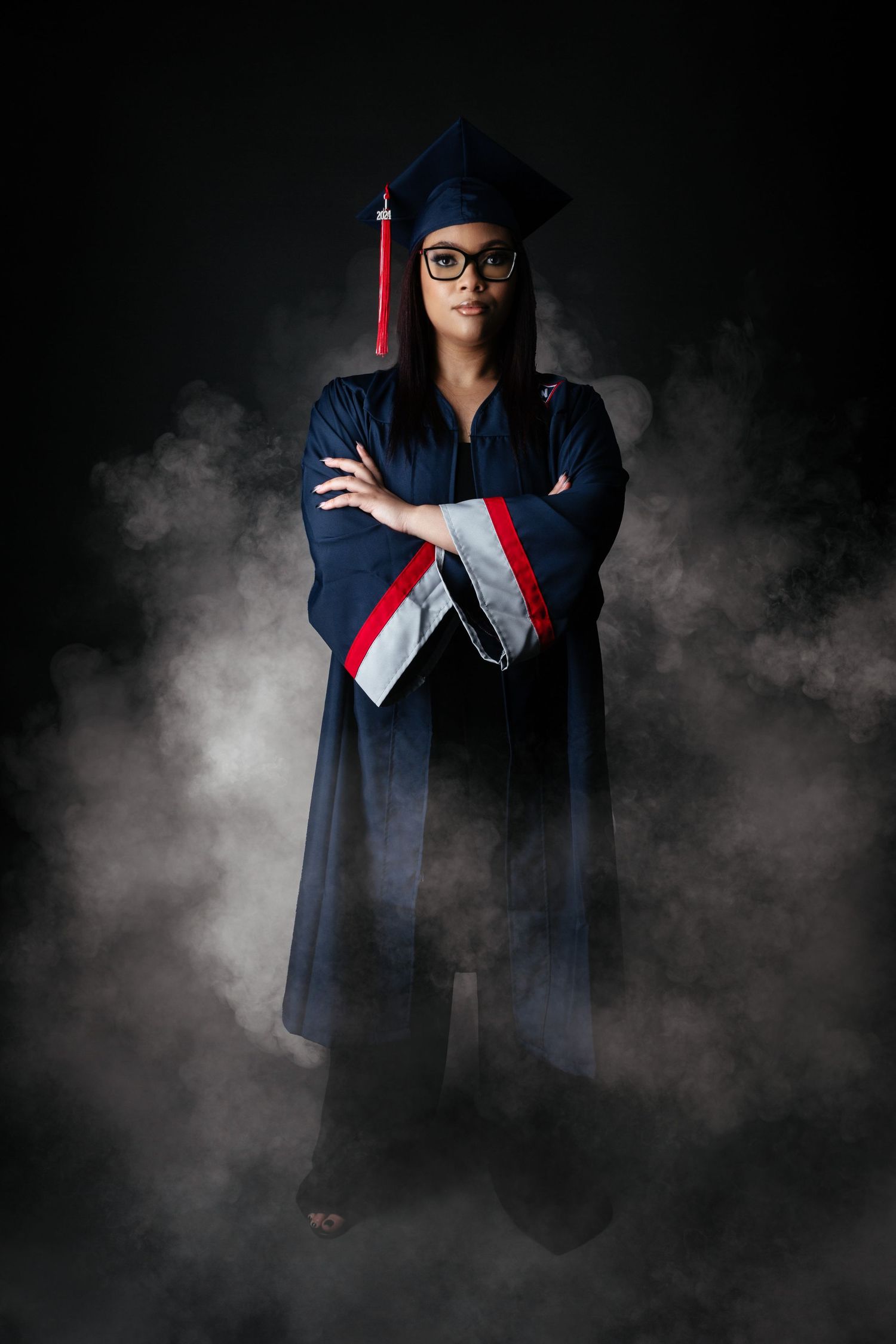 Dramatic graduation portrait with smoke effects and blue cap and gown against dark background.