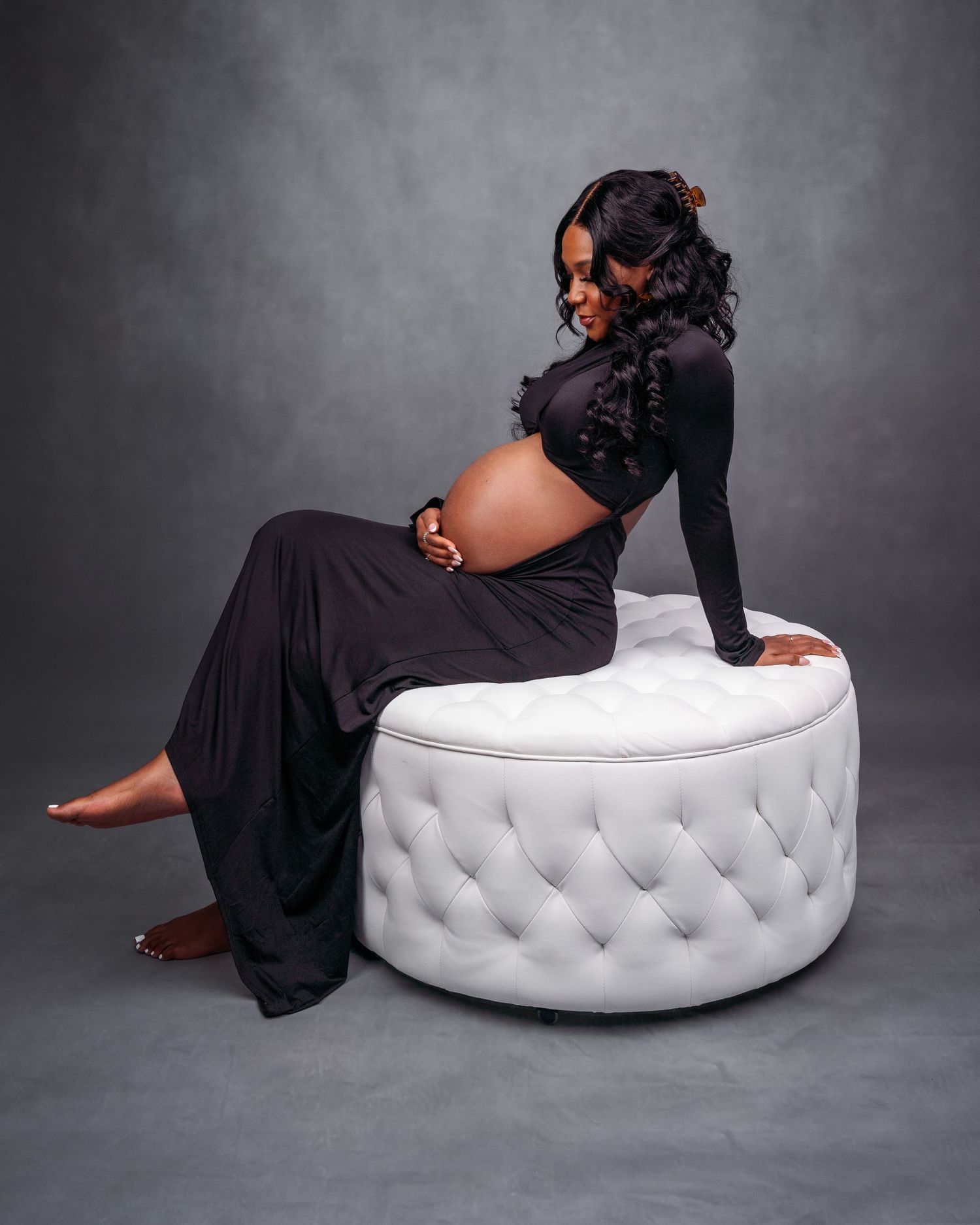 Elegant photoshoot featuring poses on a white tufted ottoman against a dark gray backdrop.