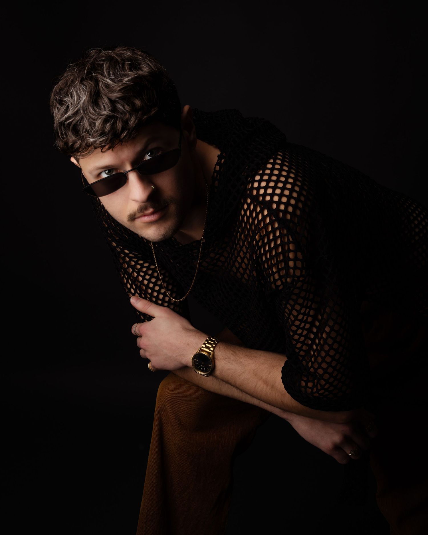 Dramatic portrait in dark lighting featuring a person wearing a mesh top and sunglasses.