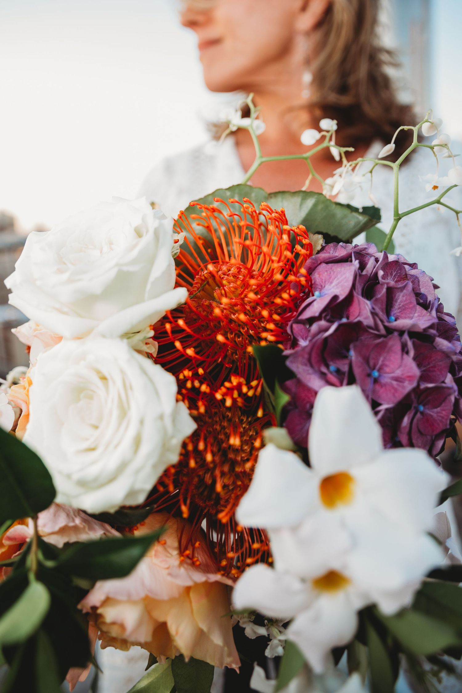 Colorful wedding bouquet featuring white roses, orange mums, and purple hydrangeas.
