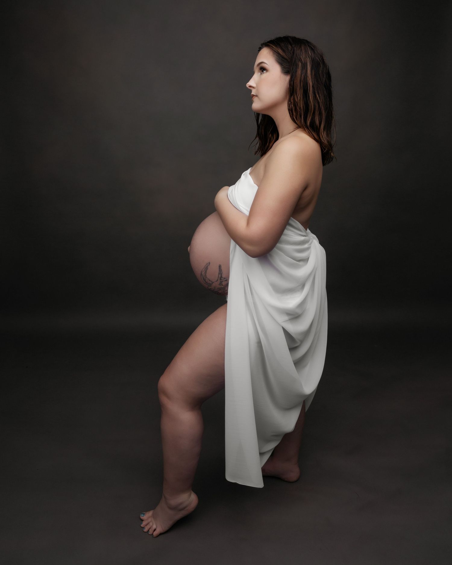 Minimalist maternity portrait with white draping fabric against black backdrop.
