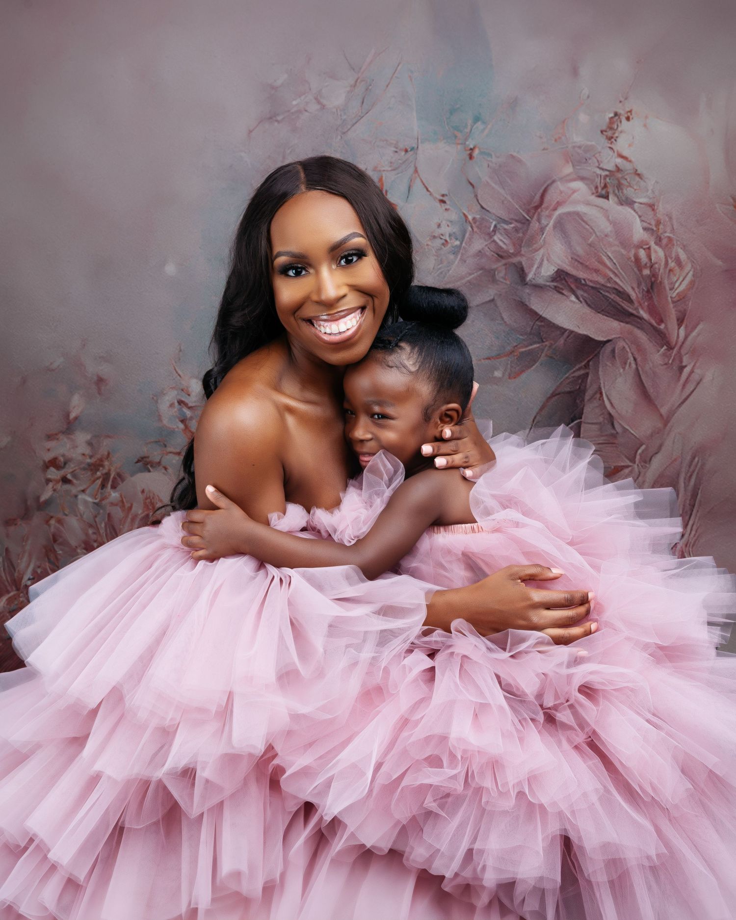 Mother and child share tender moments in matching pink tulle gowns against a romantic backdrop.