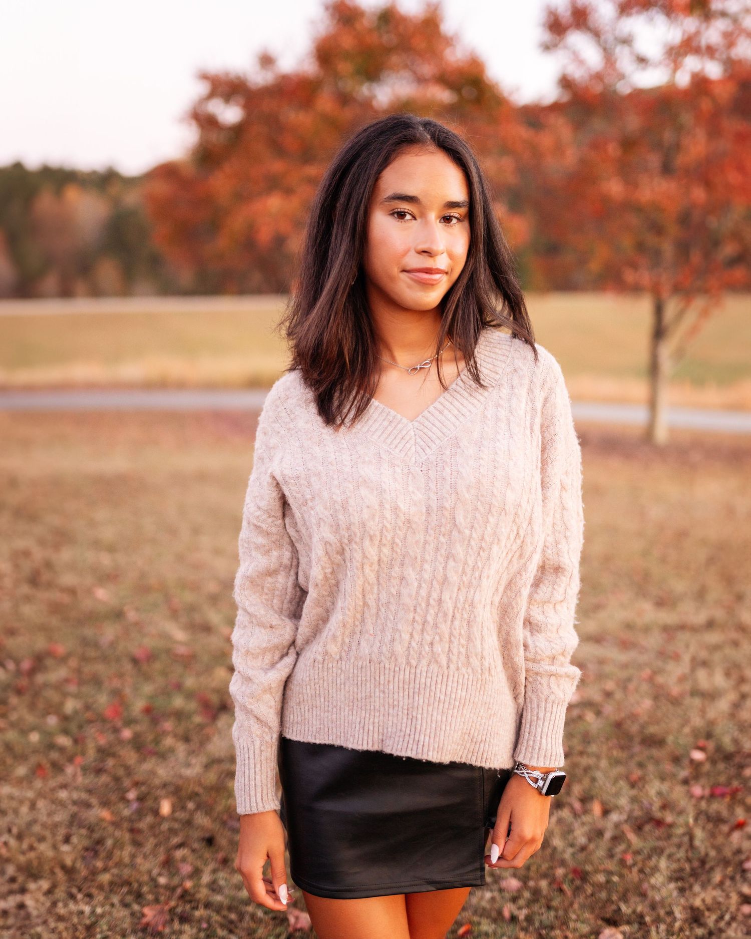 Fall fashion portrait featuring cream sweater and black shorts against autumn foliage.