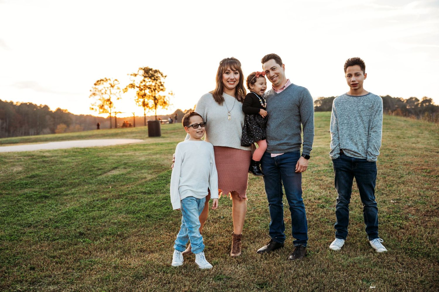 A family poses together outdoors during a golden hour photo session.
