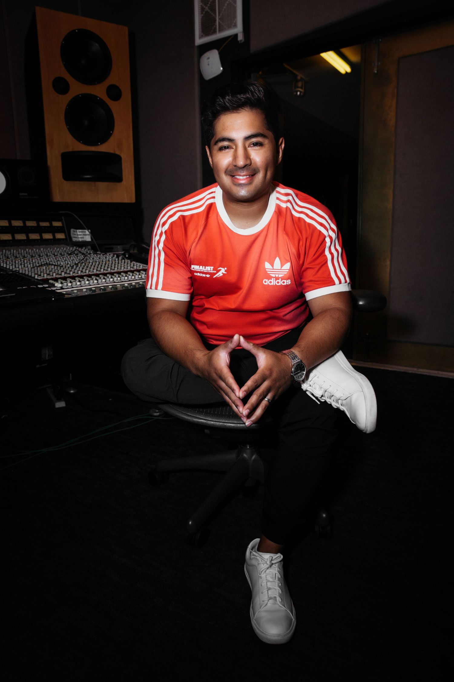 Person wearing red Adidas sportswear sitting in dark room with studio lighting.