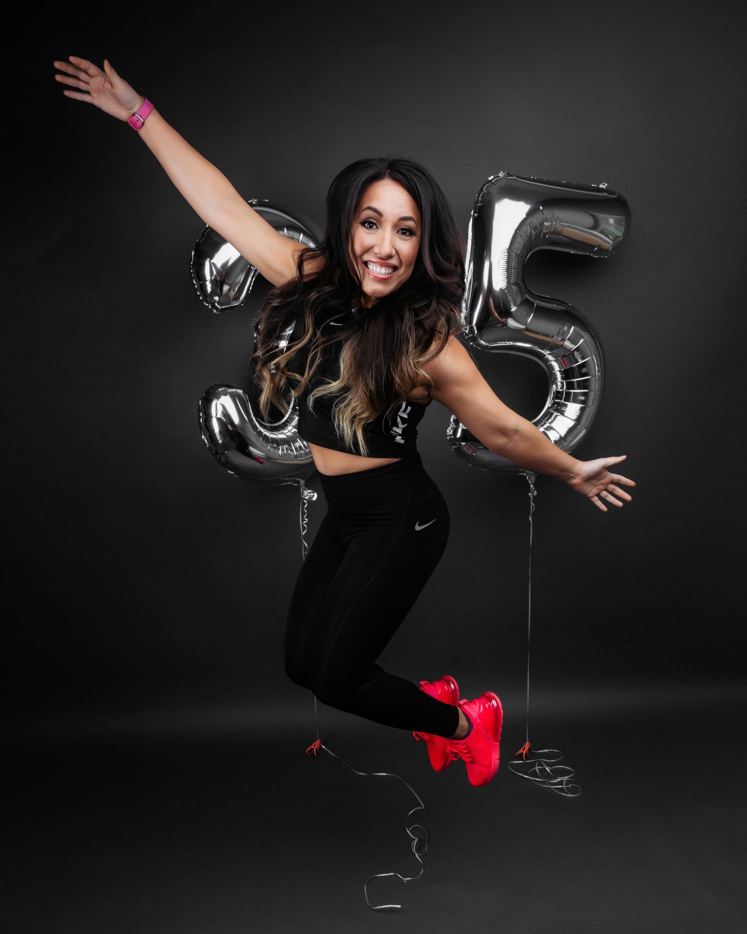 Dynamic fitness photoshoot with person in black workout gear and red shoes against dark background.