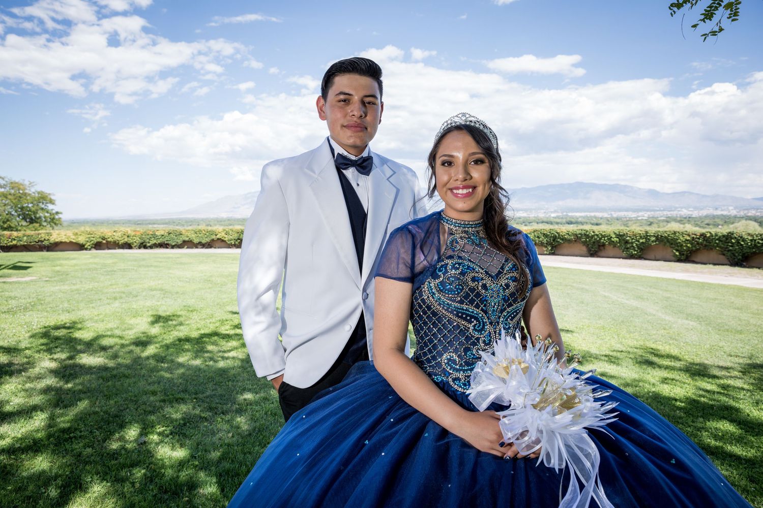 Quince party members in formal attire pose outdoors against a scenic landscape.