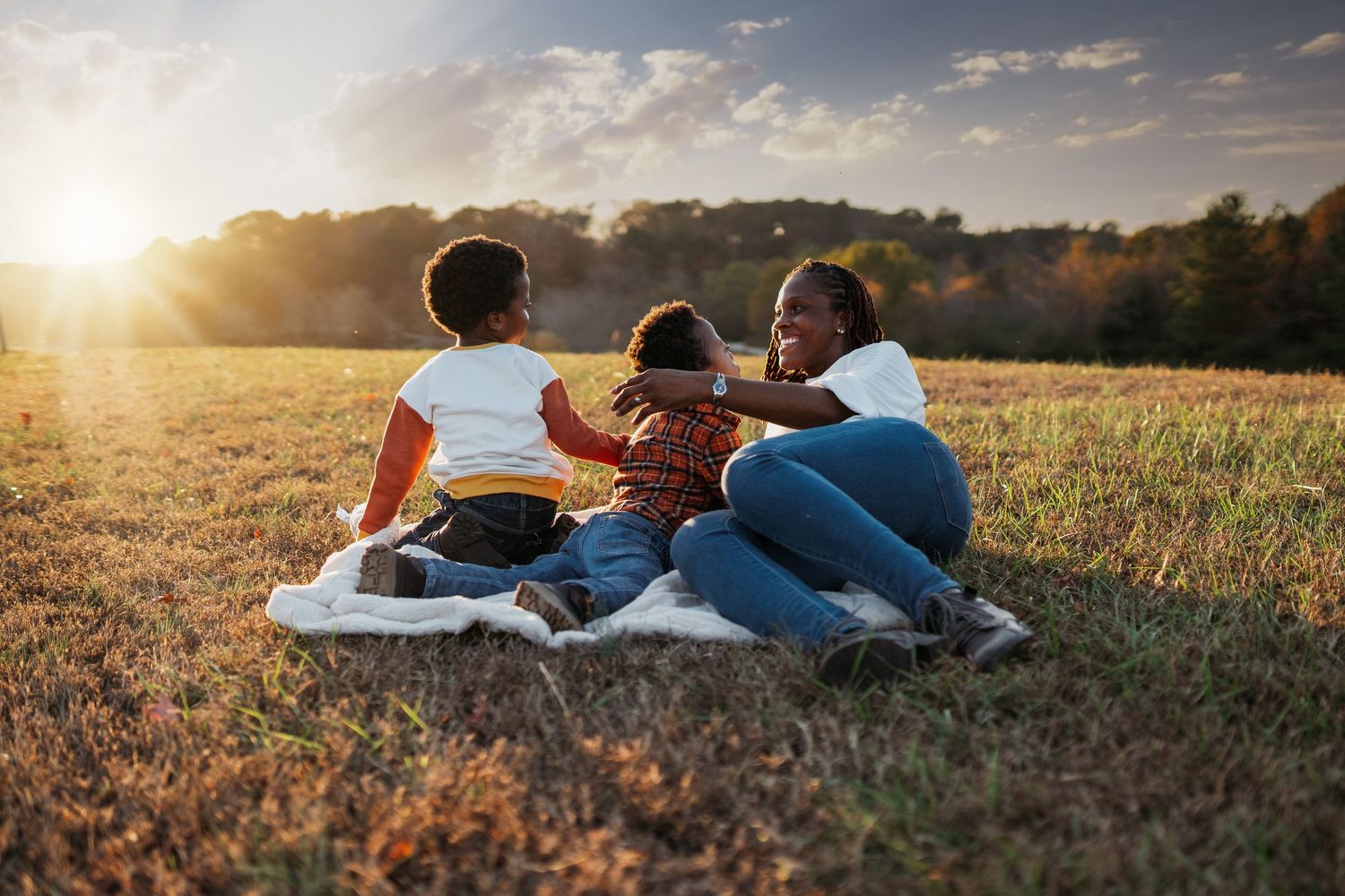 Group relaxing together on blankets in a grassy field at sunset.