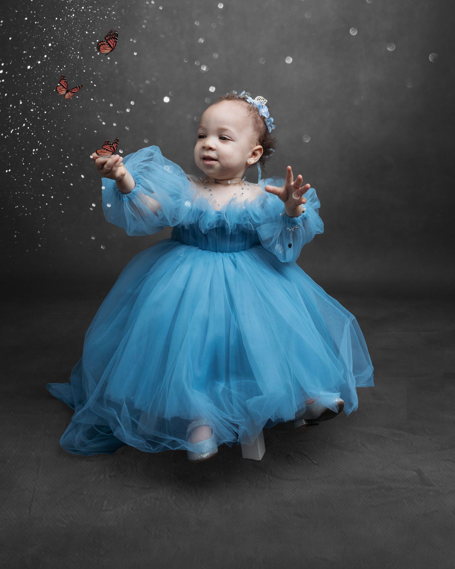 Baby in flowing blue tulle dress with sparkles in magical studio portrait.