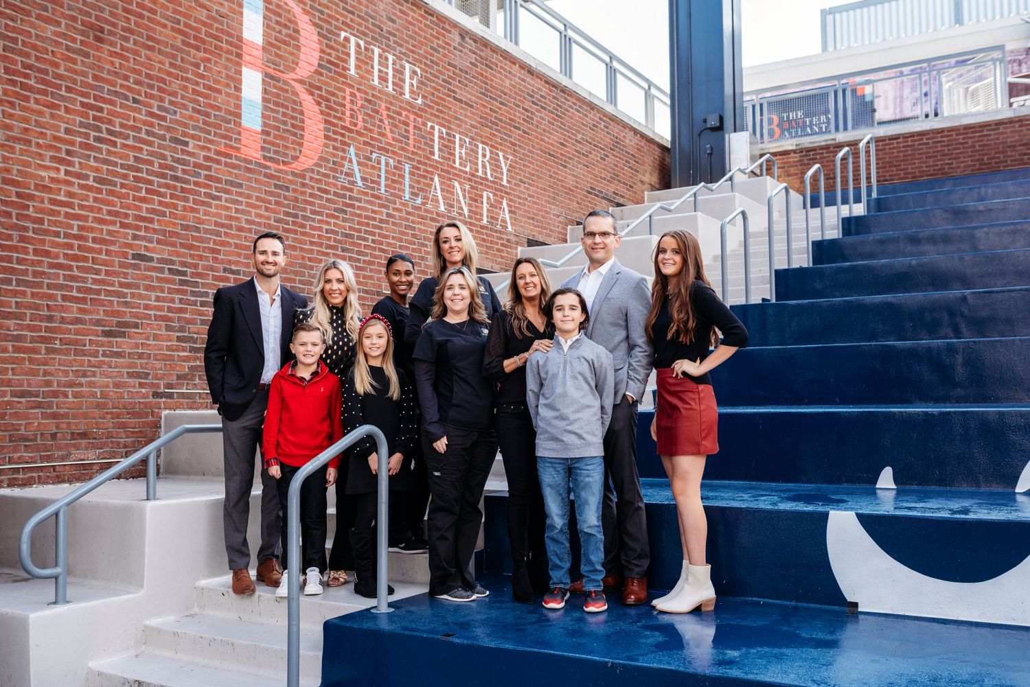 A group stands together on blue steps outside a brick building with The Battery signage.