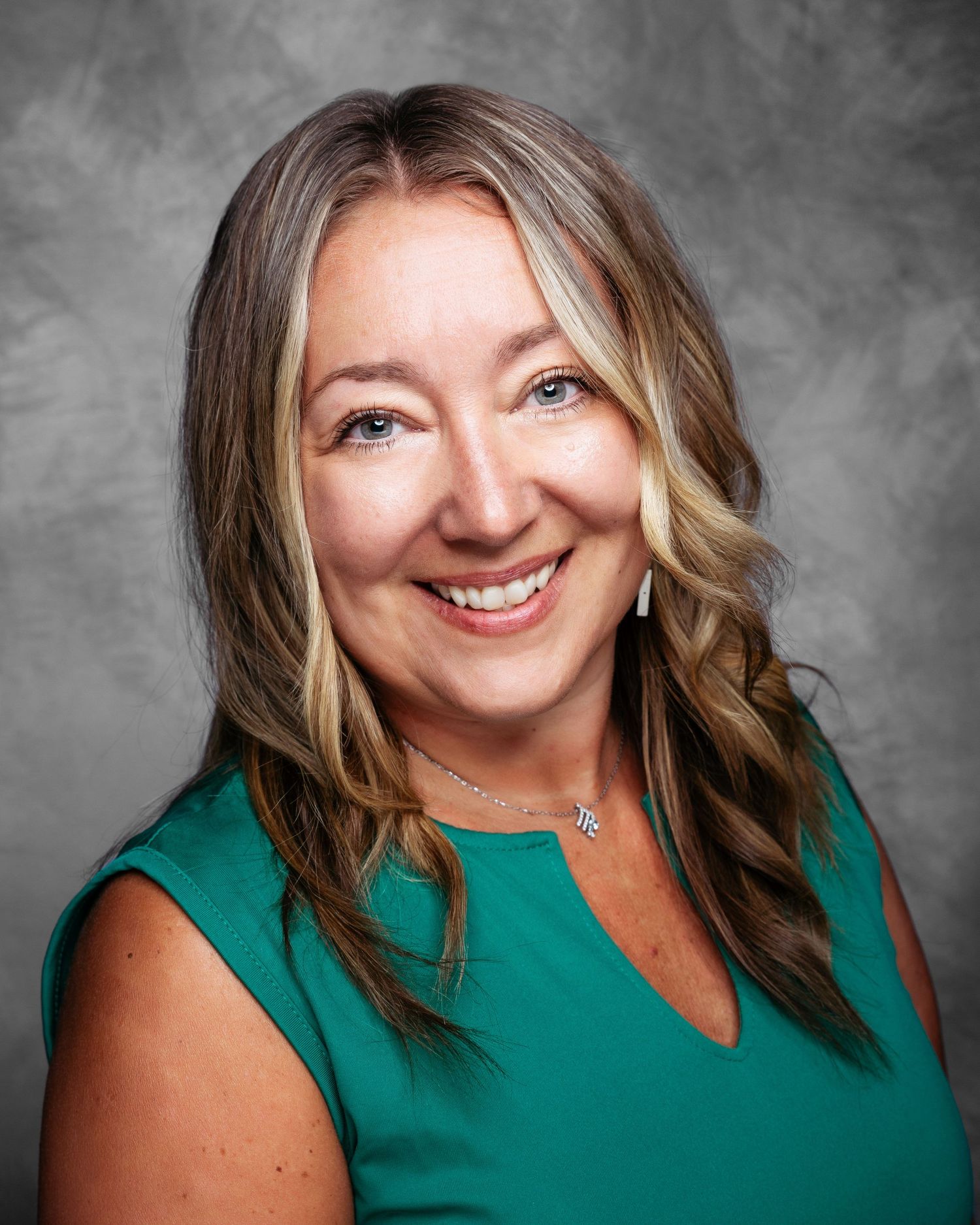 Professional headshot of a person wearing a green sleeveless top against a gray background.