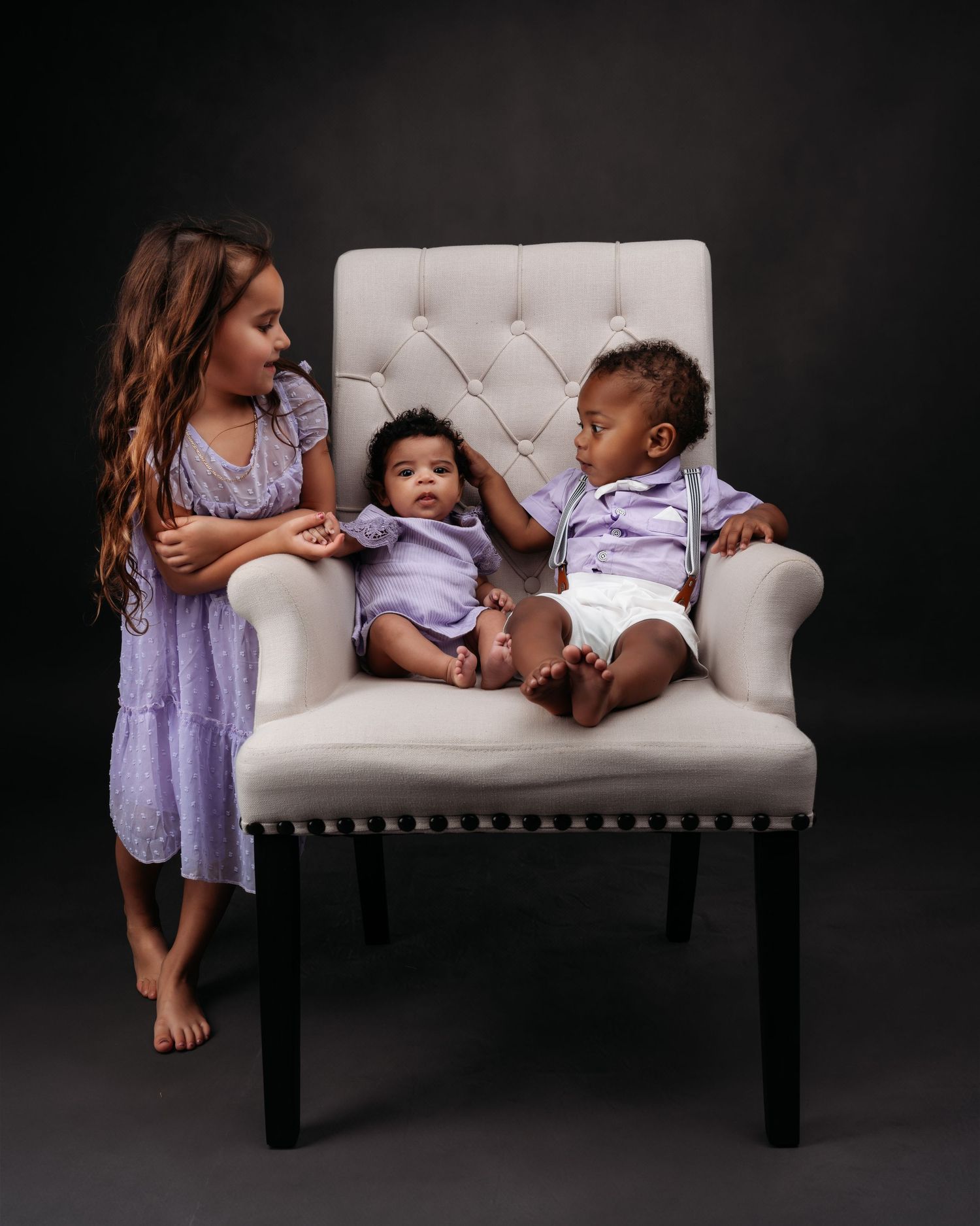Children lounging on white tufted bench during studio photo session.