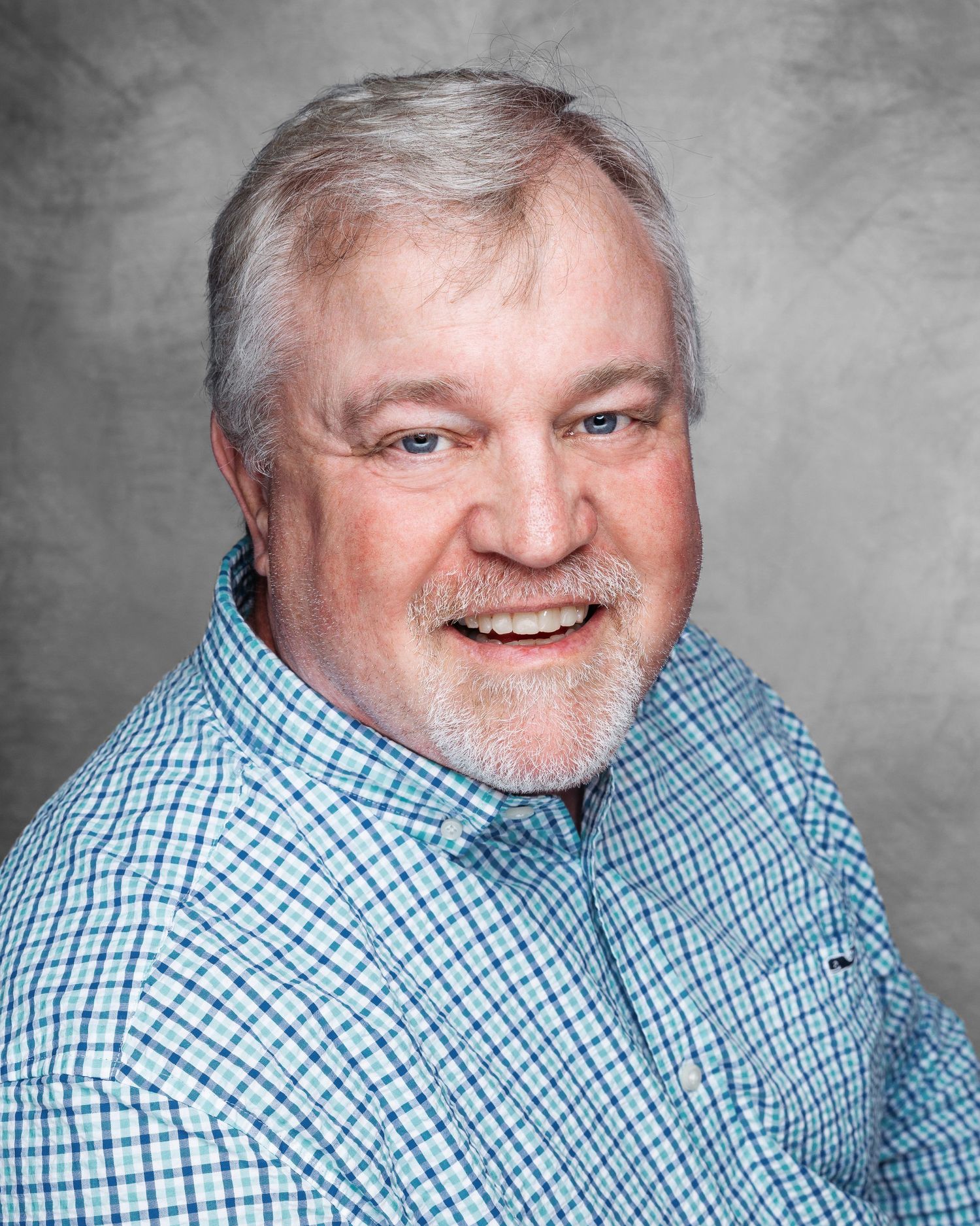 Professional headshot of a person wearing a blue checkered shirt against a gray background.