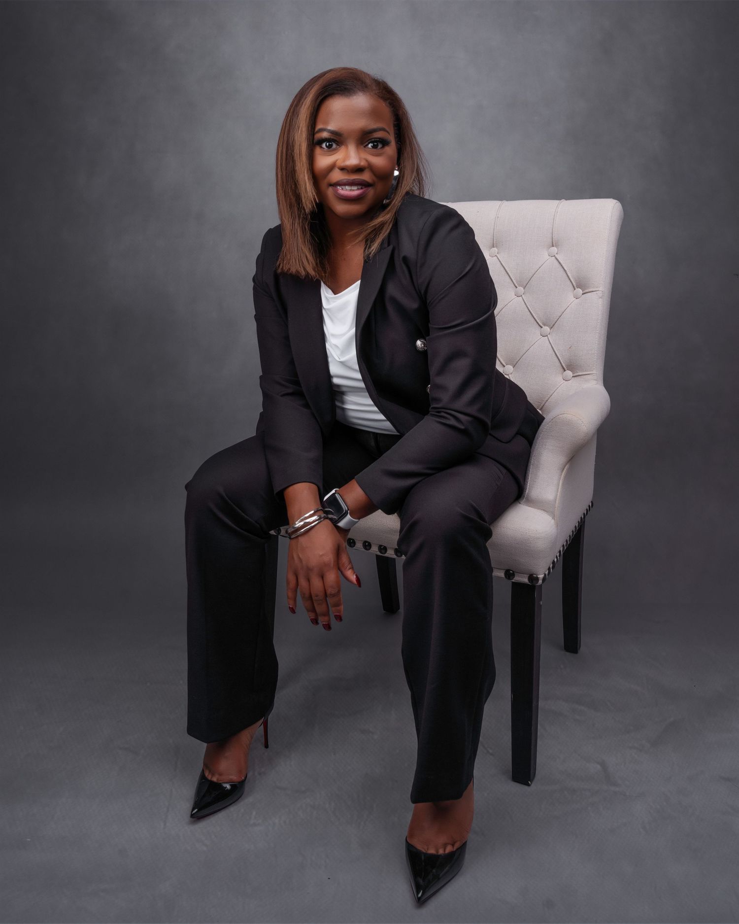 Professional studio portrait featuring business attire and a grey tufted chair.