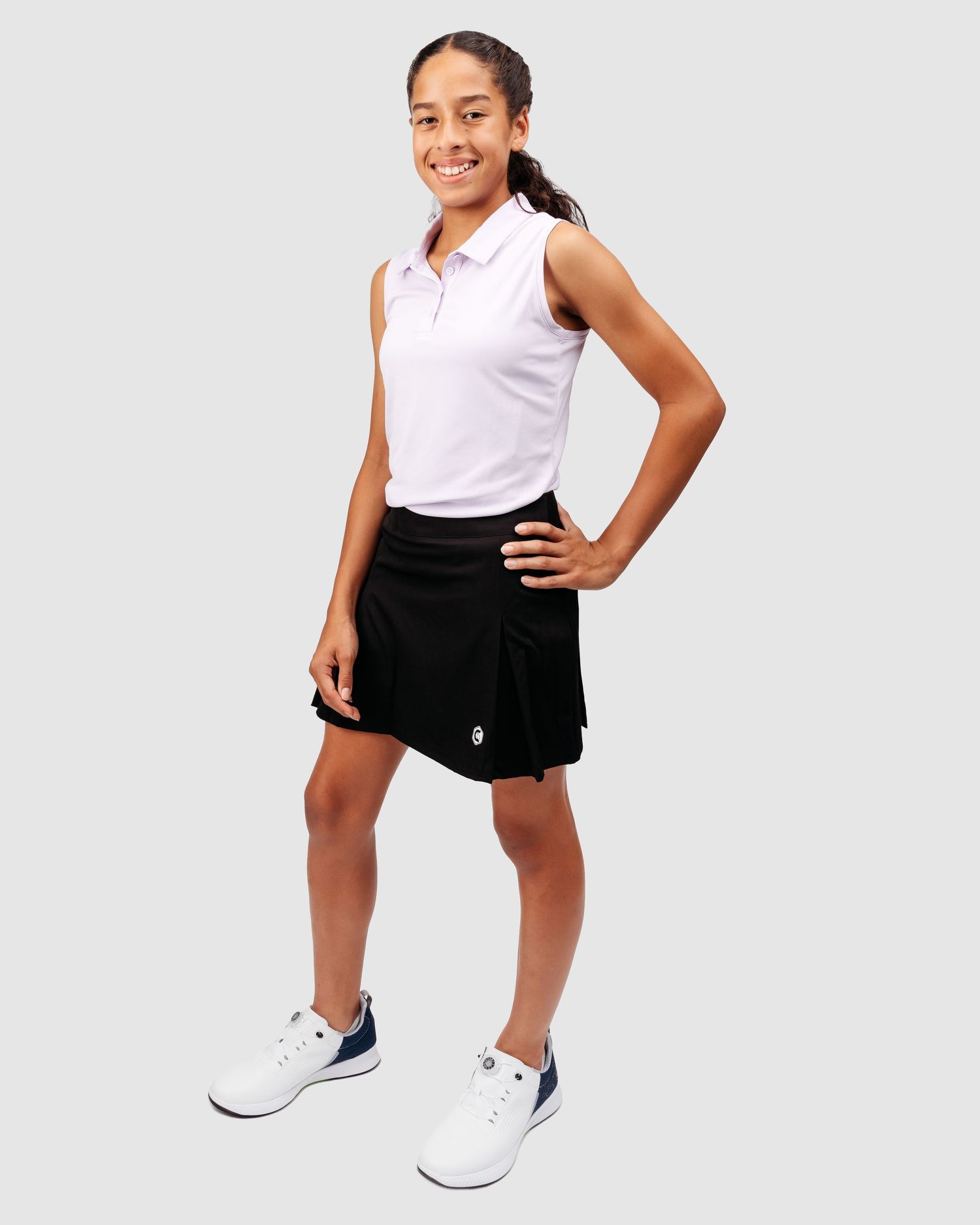 Young athlete in white polo and black shorts demonstrates golf stance.