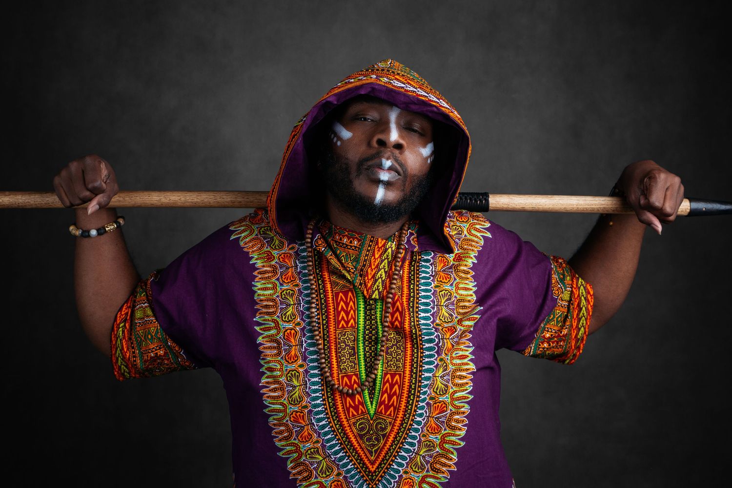 Person wearing colorful African dashiki poses dramatically against dark background.