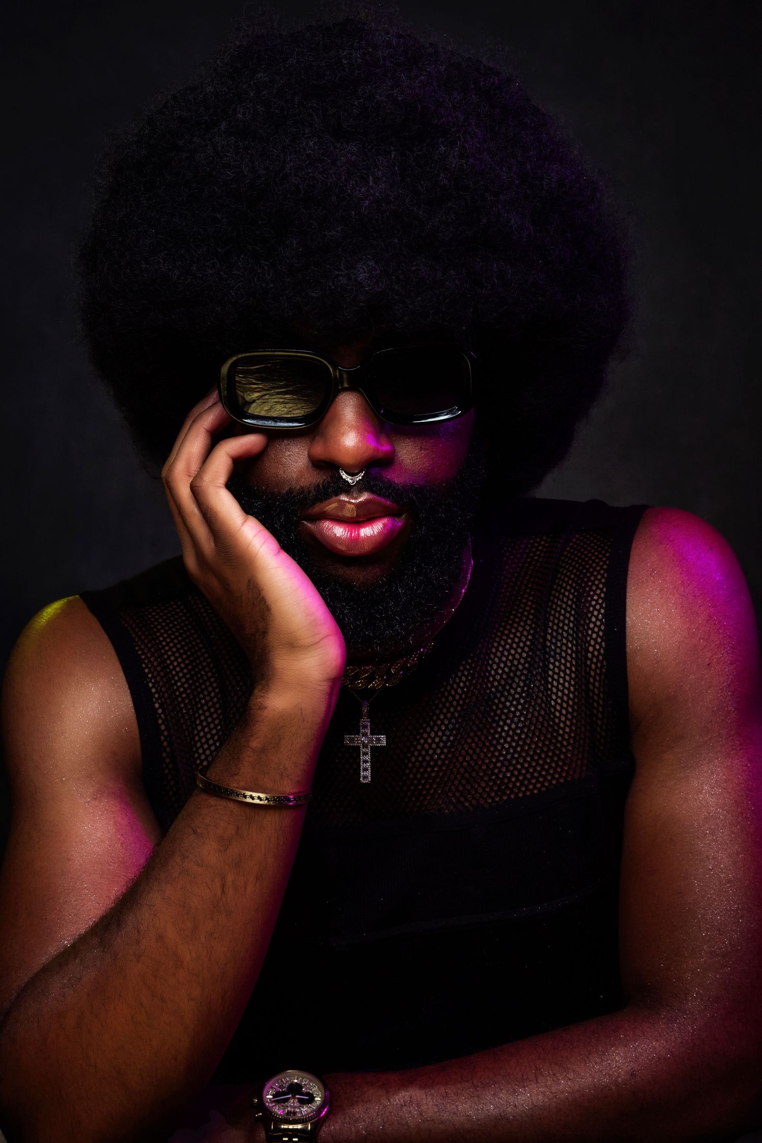 Dramatic portrait with afro hairstyle, sunglasses and mesh top in colorful lighting.