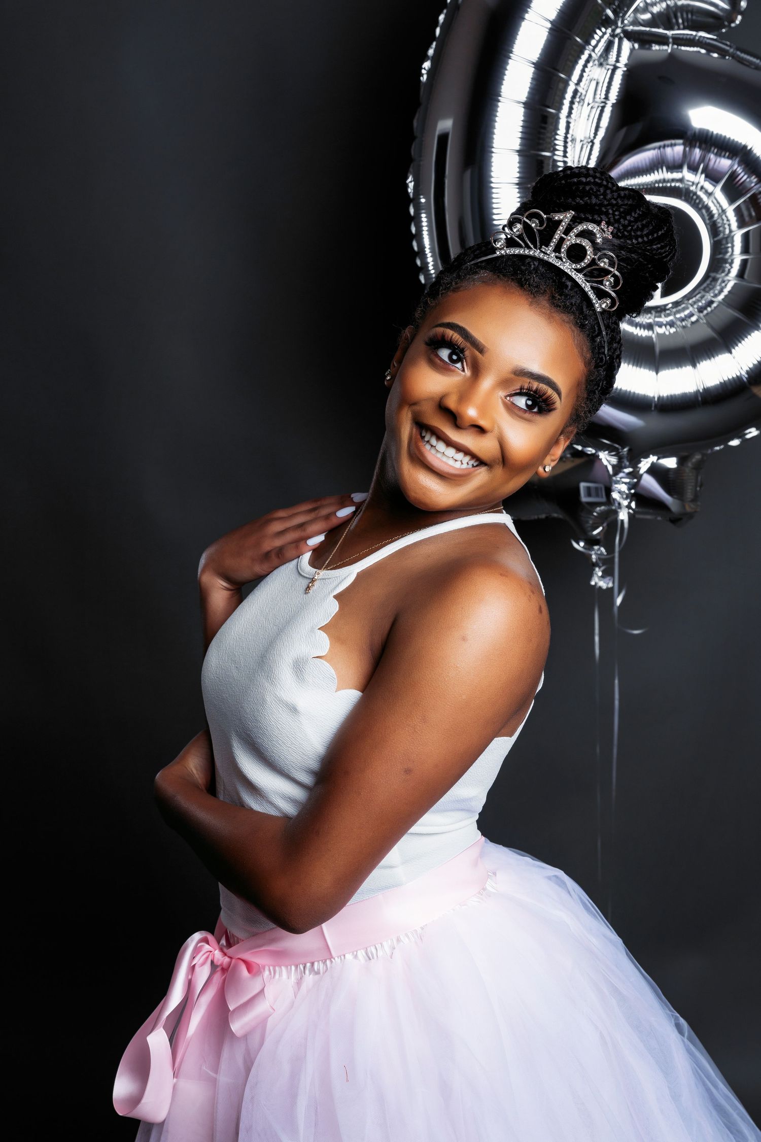 Celebratory portrait session with silver balloons and white tulle dress against dark backdrop.