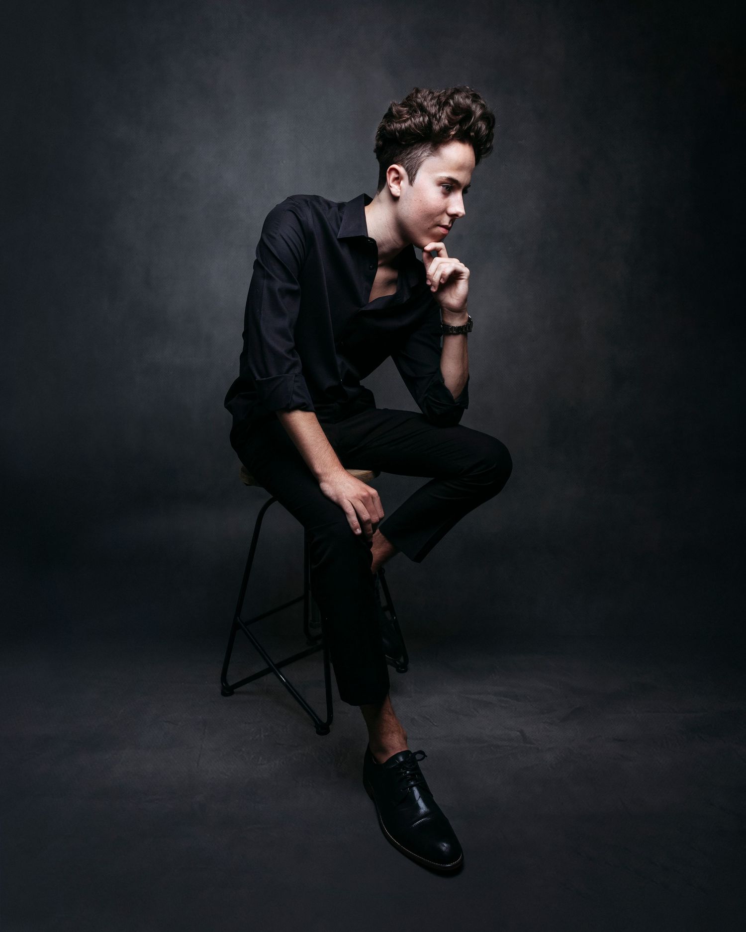 Dramatic black and white portraits of a person in dark attire seated on a chair in various poses.