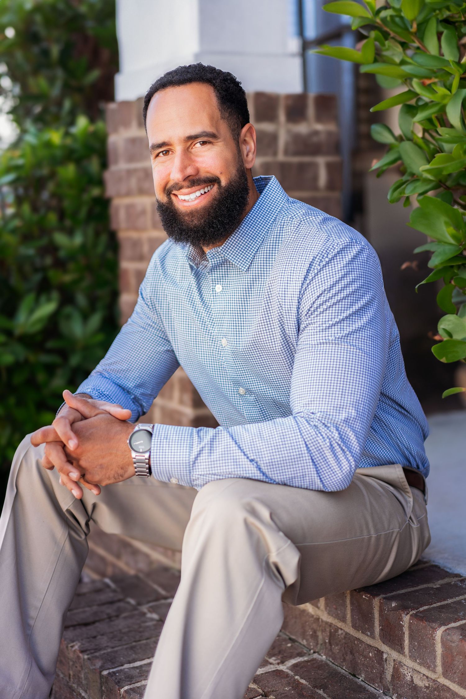 Casual portraits of person sitting on brick ledge wearing blue checkered shirt.