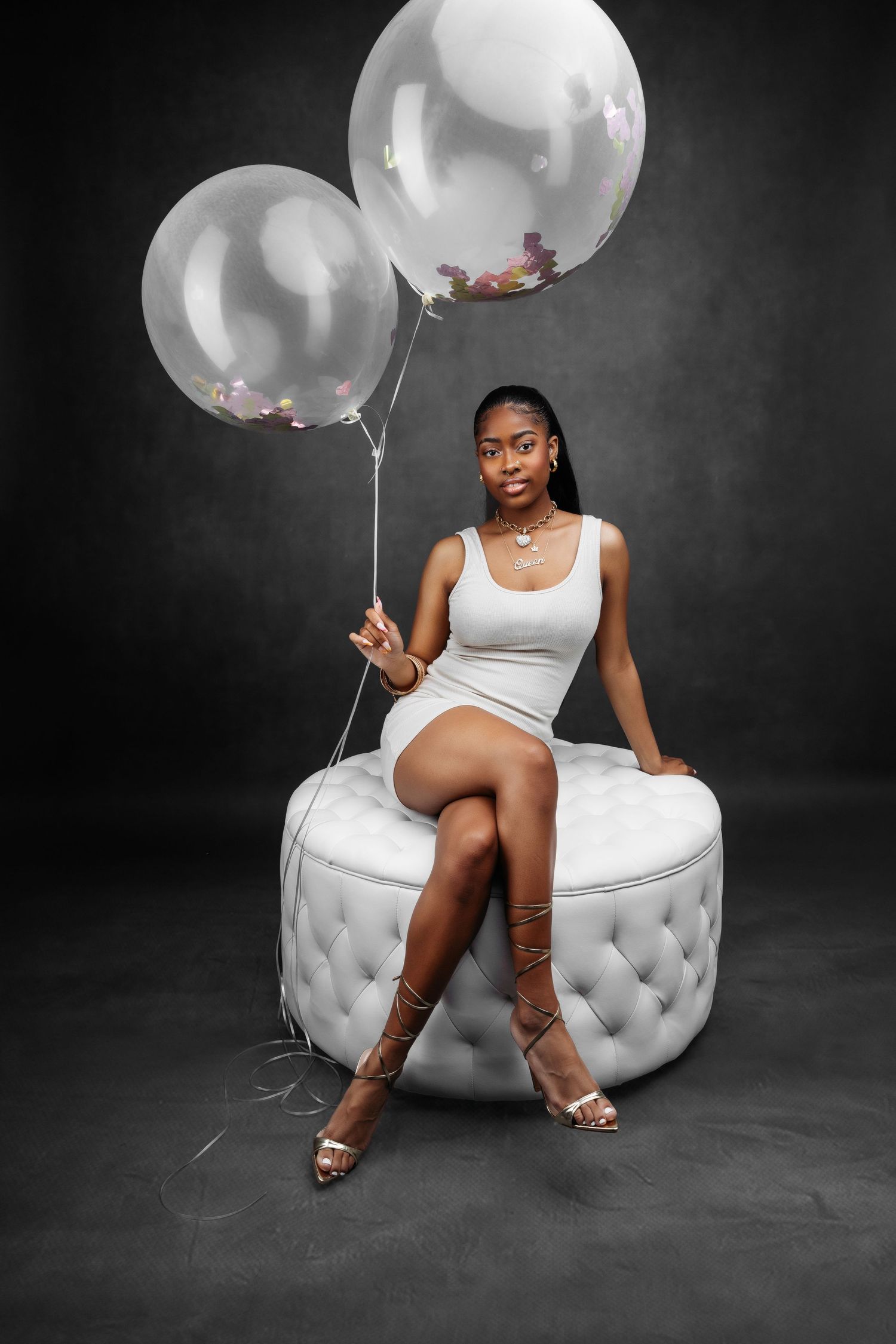Elegant portrait session featuring a white tufted ottoman and ethereal white balloons against dark backdrop.