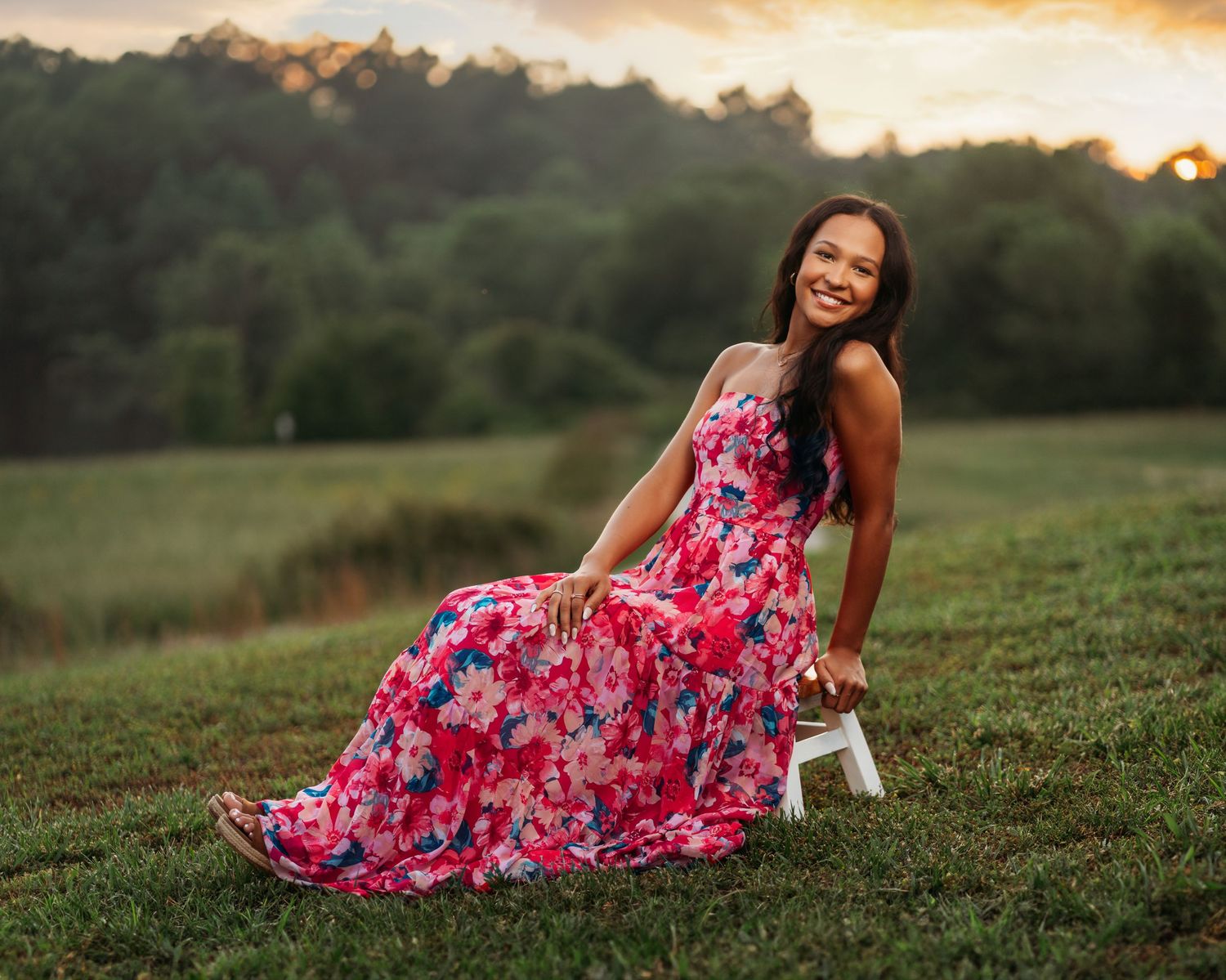 Someone wearing a vibrant floral dress poses in a field during golden hour.