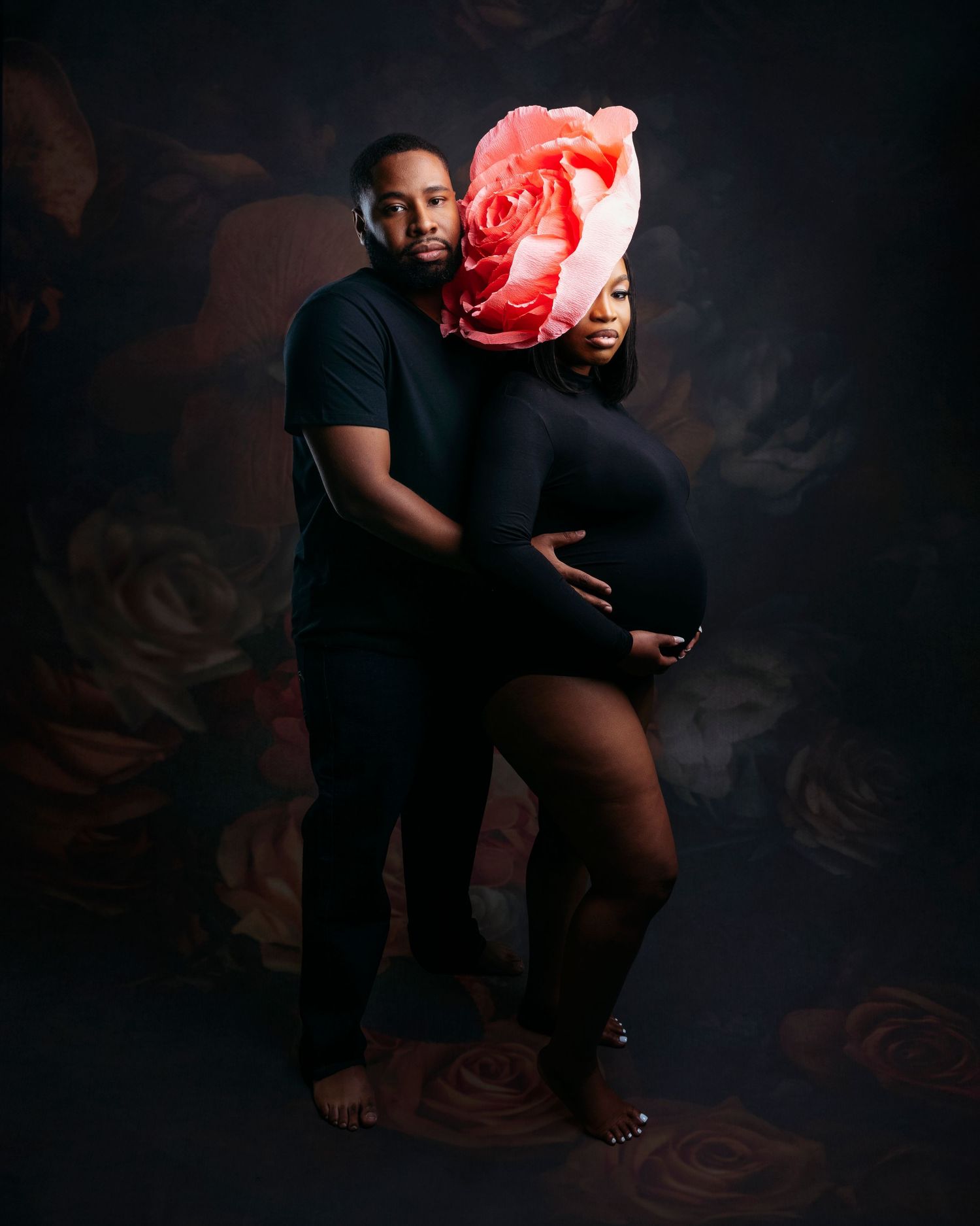 Artistic maternity photo shoot with couple in black attire holding red heart prop.