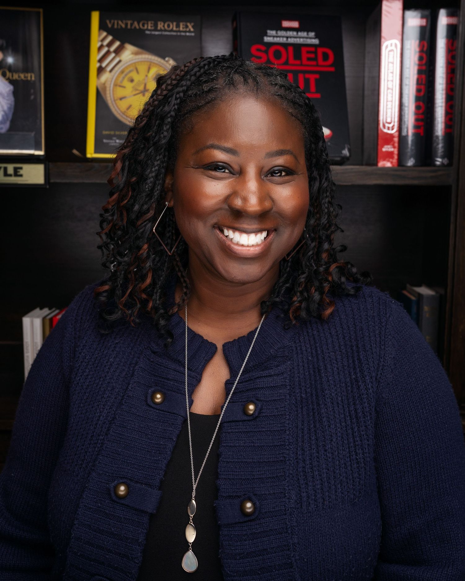 Person in navy sweater smiling against dark background with vintage posters.