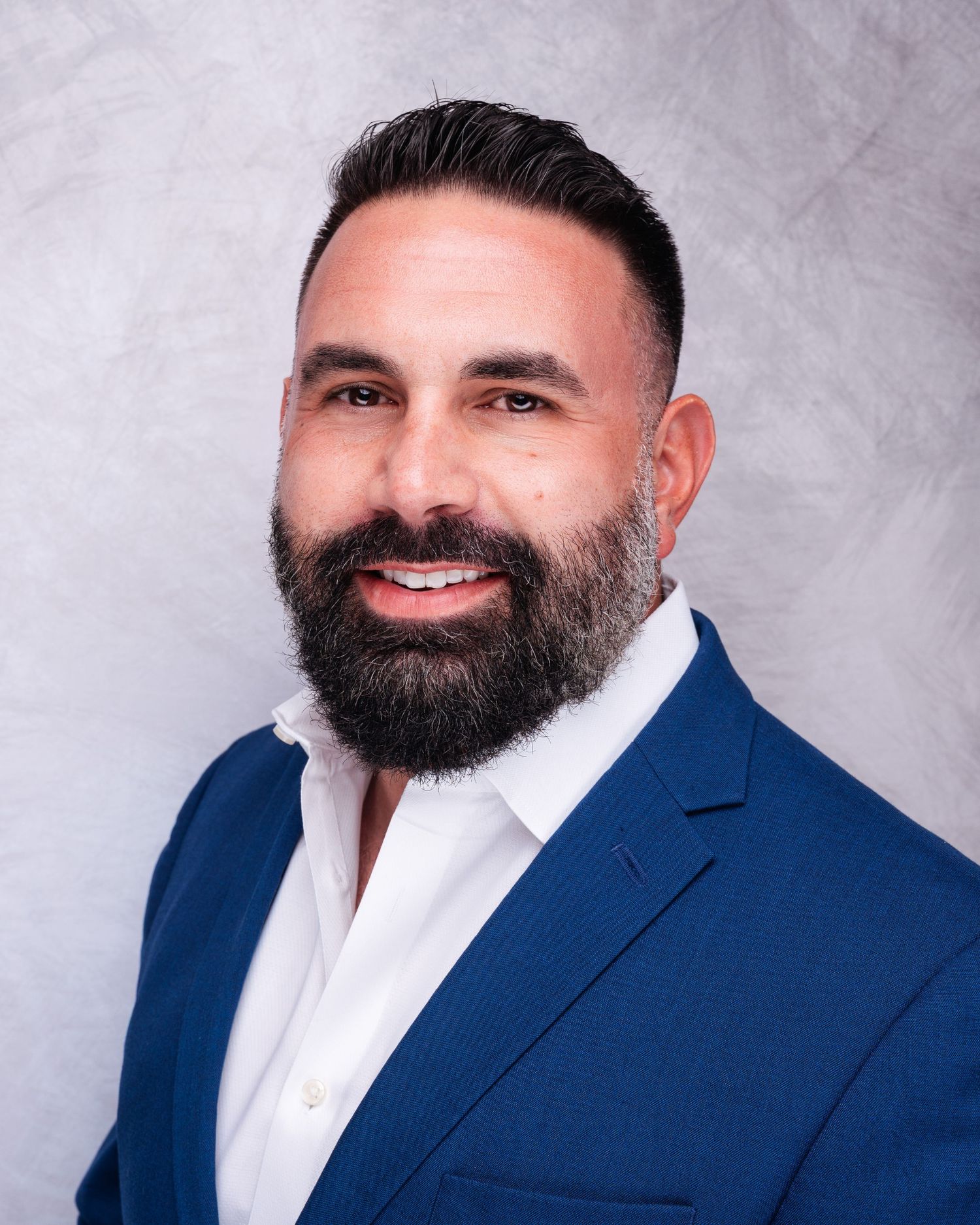 Professional headshots of person in navy suit and white shirt against gray background.