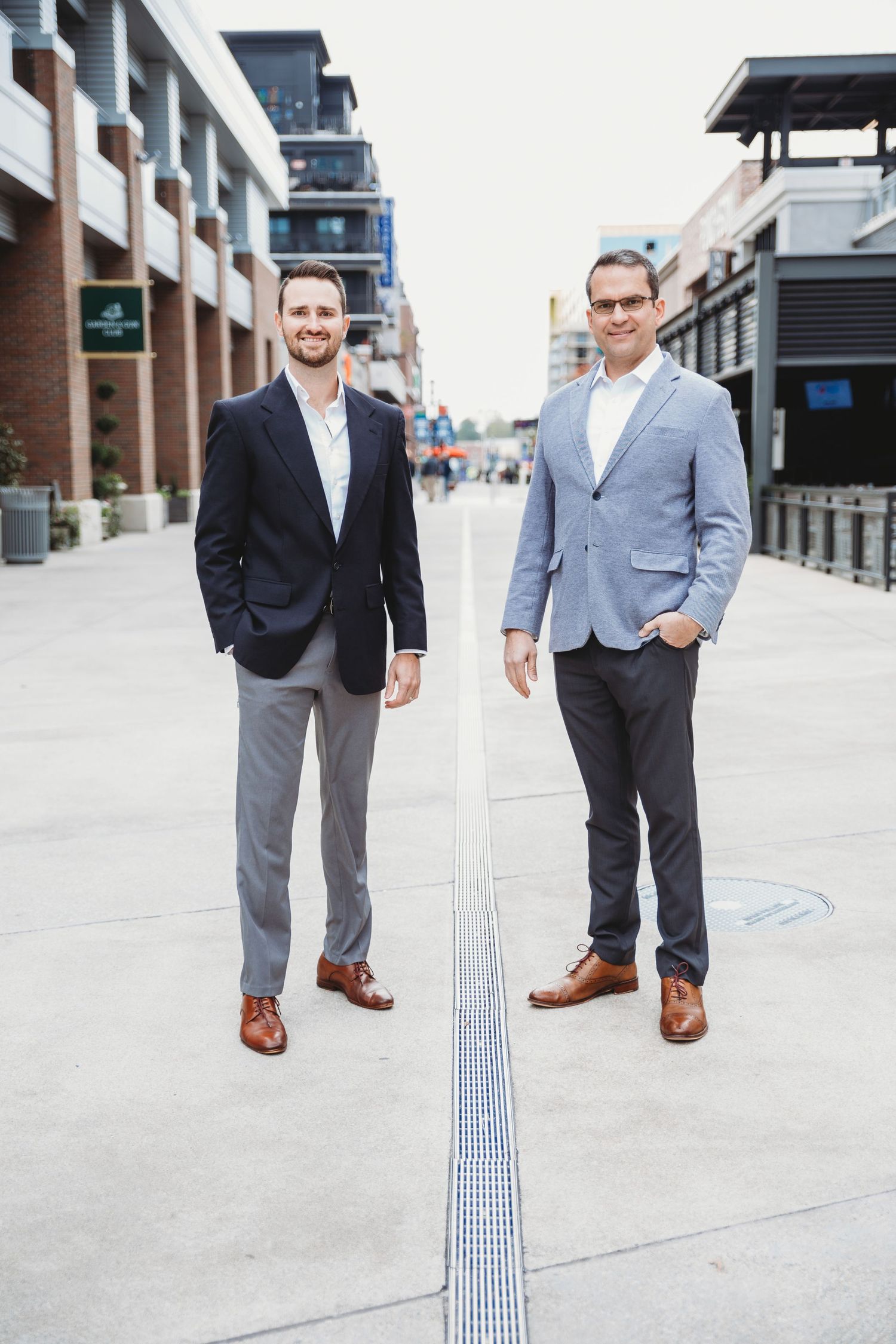 Two businessmen in blazers standing on opposite sides of linear ground feature in urban setting.