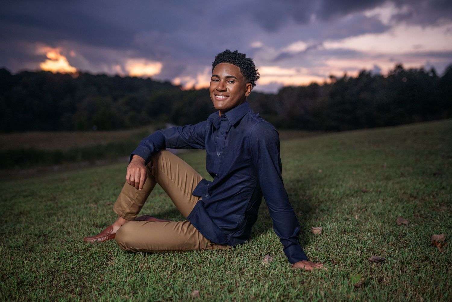 Casual outdoor portrait session on grassy field during dramatic sunset.