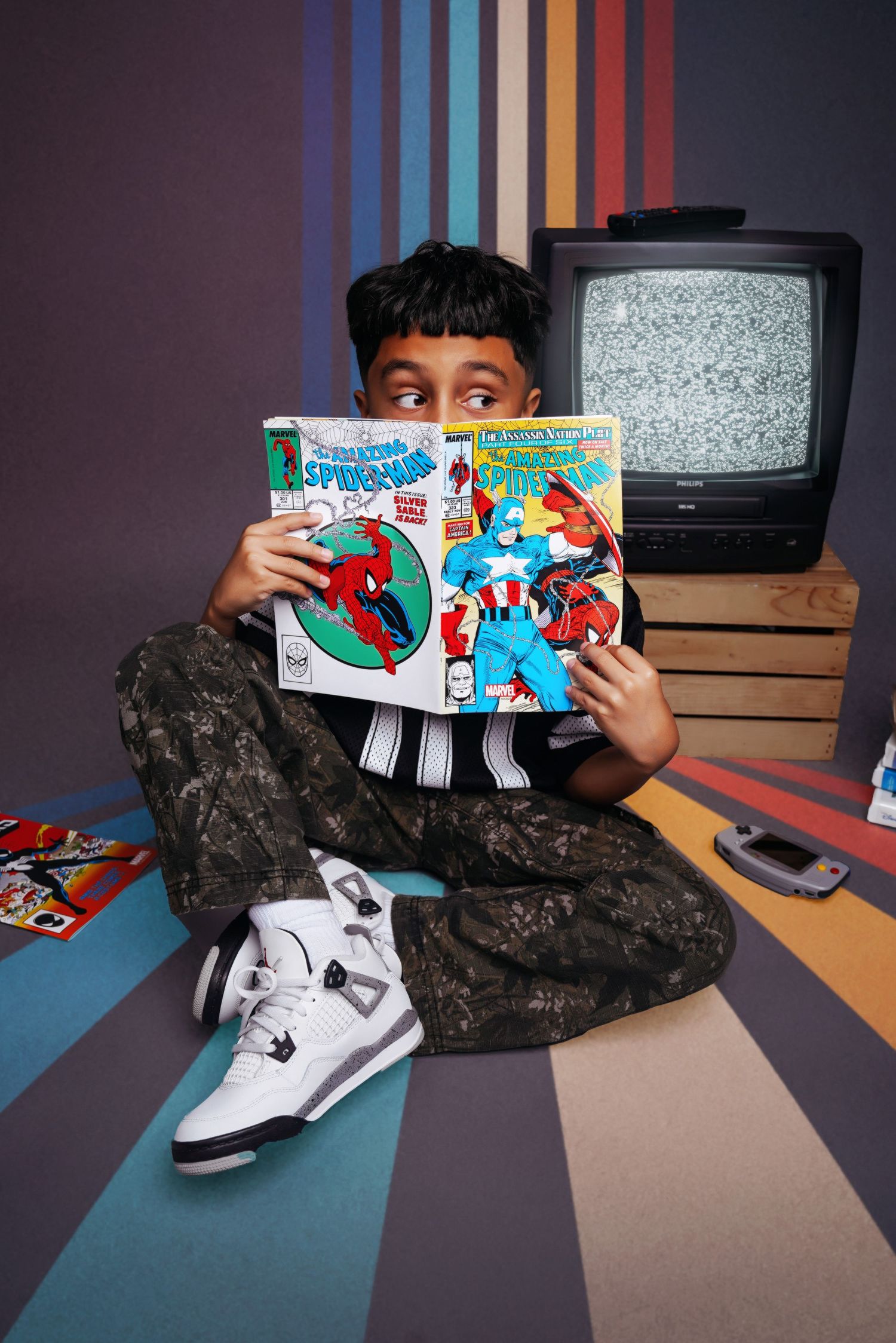 Child lying on floor with sneakers and comic books in a casual indoor setting.